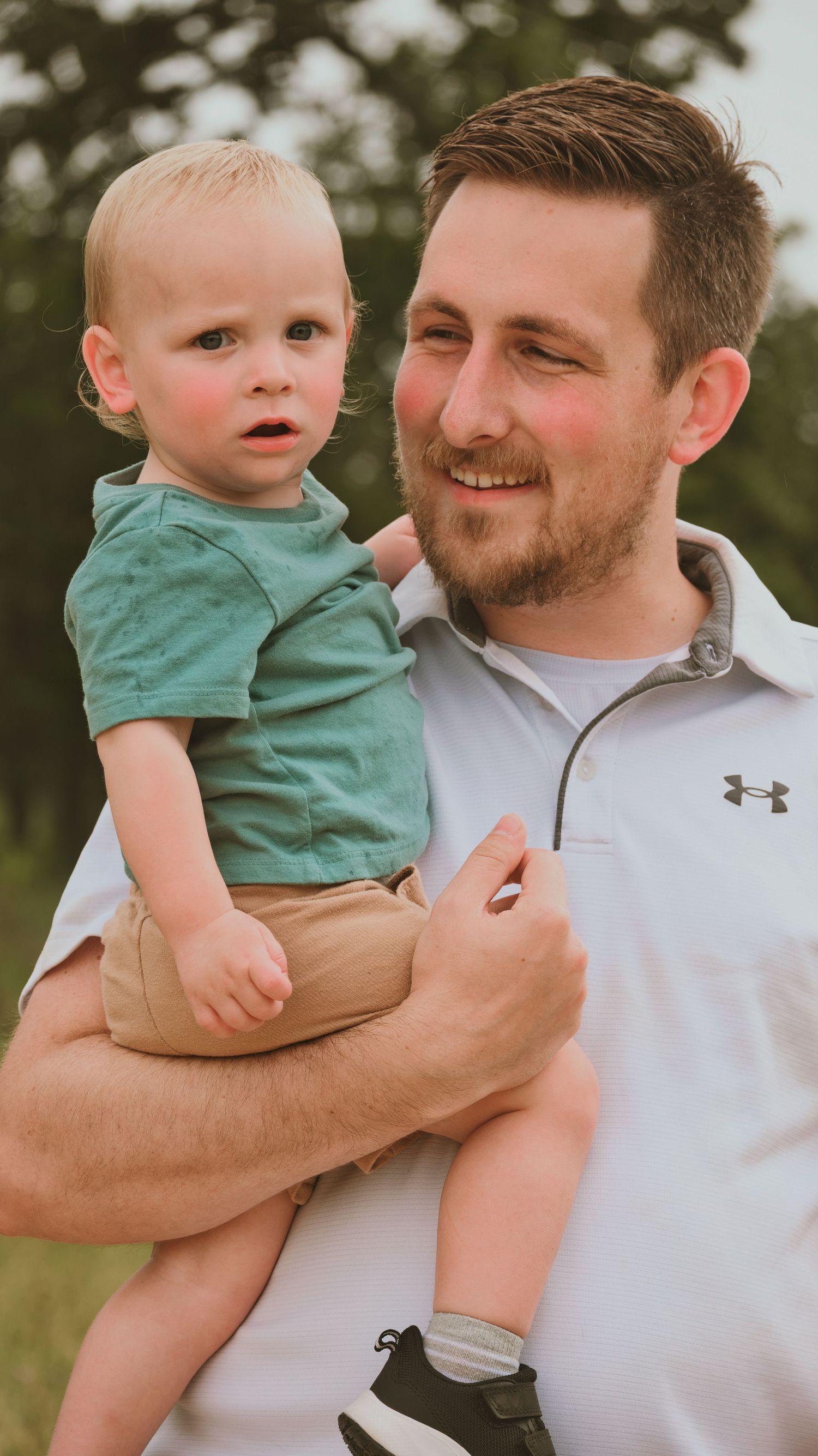 Smiling father holding his young blonde toddler son during an outdoor family portrait session.