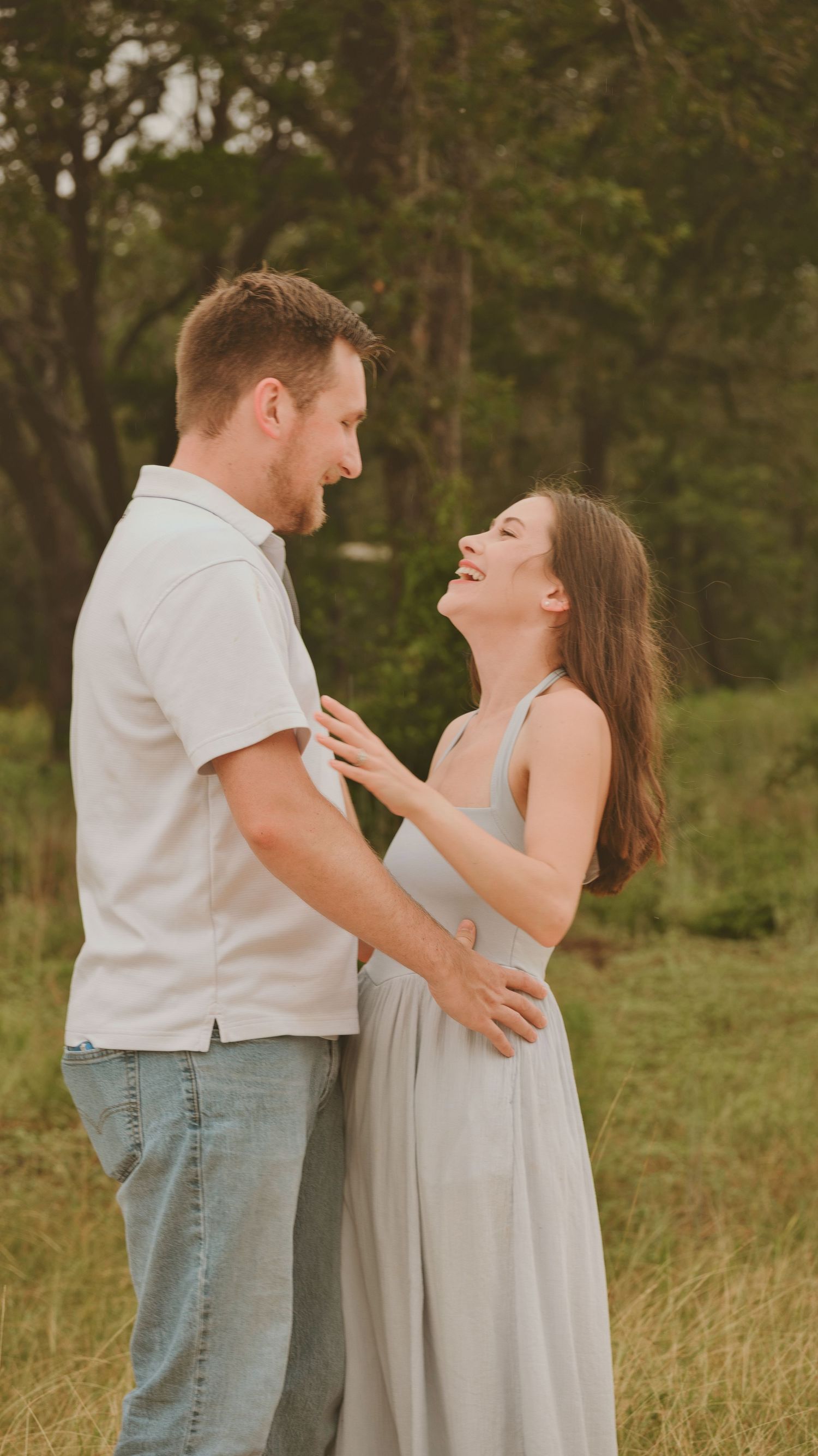 Happy couple laughing and embracing in a green meadow during golden hour for a family session.