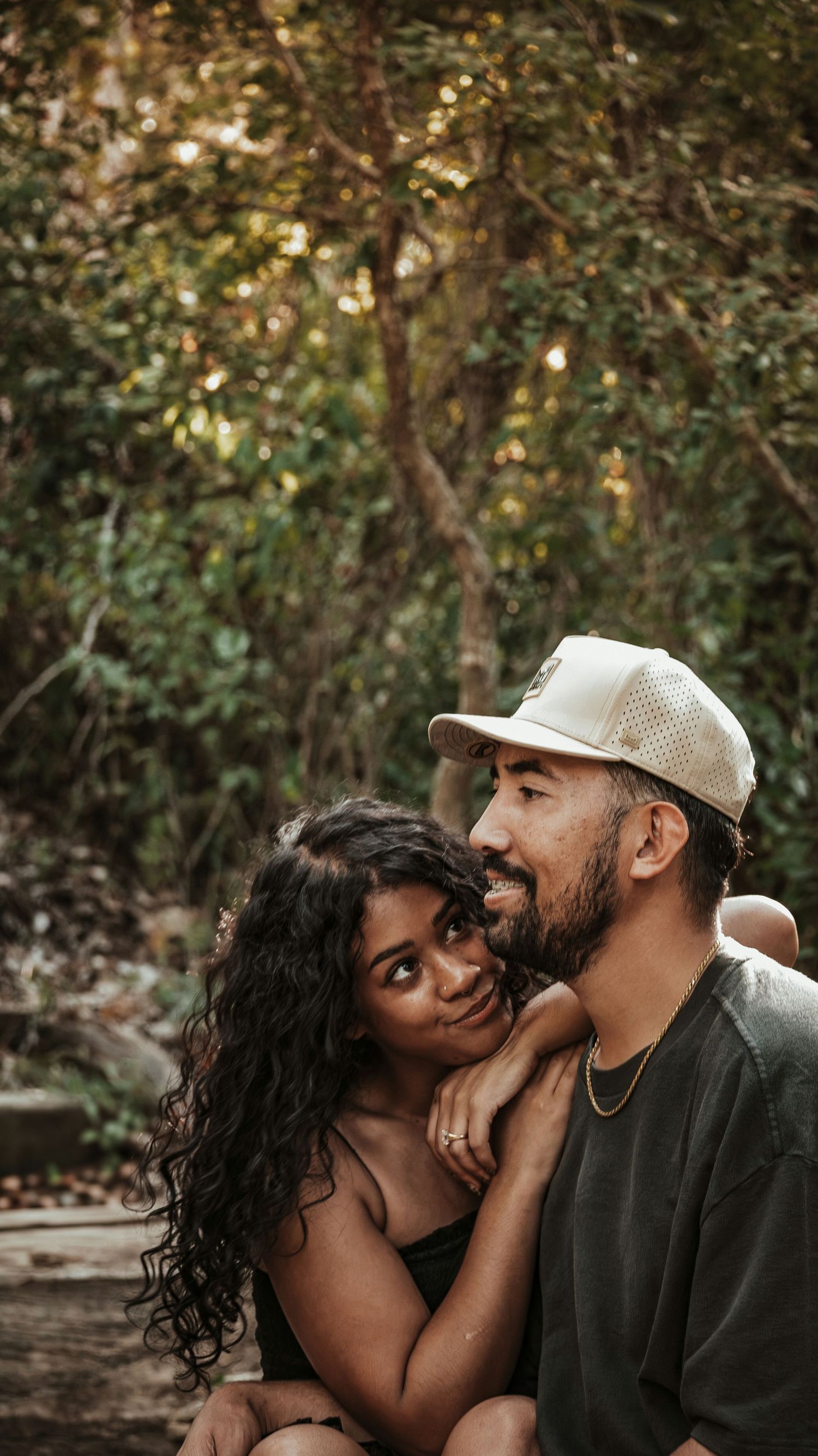 Couple embracing in a forest, woman with curly hair resting her head on a smiling for a couples session.