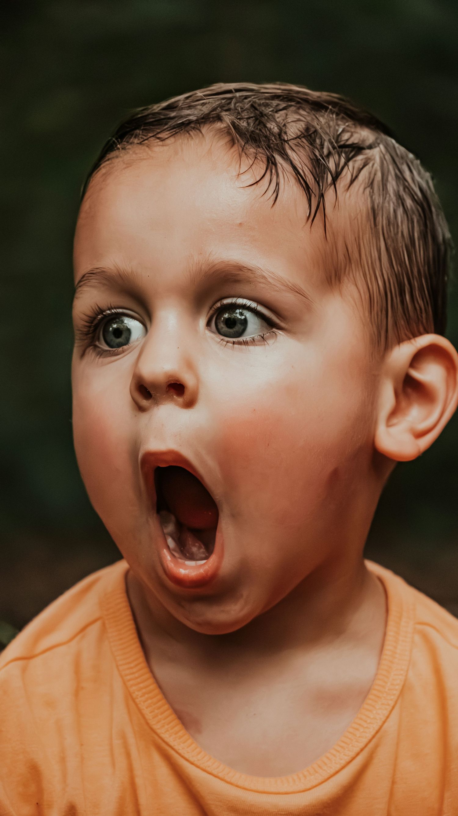 A young boy in an orange shirt with wide eyes and an open mouth showing a surprised expression.