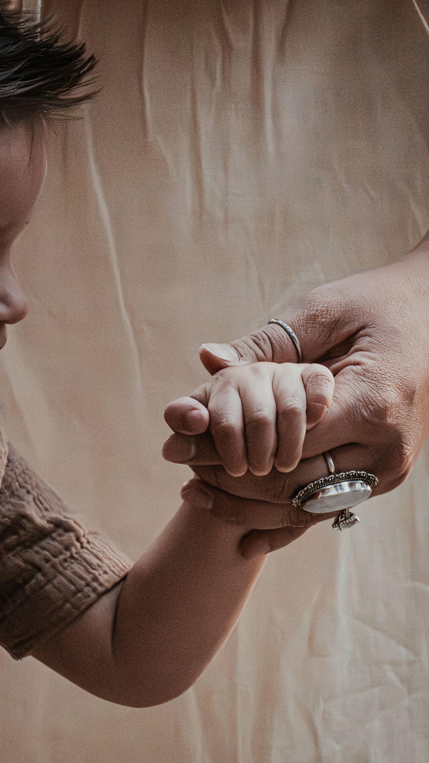 Close-up of mother's ringed hand tenderly holding her baby's tiny hand against soft background.