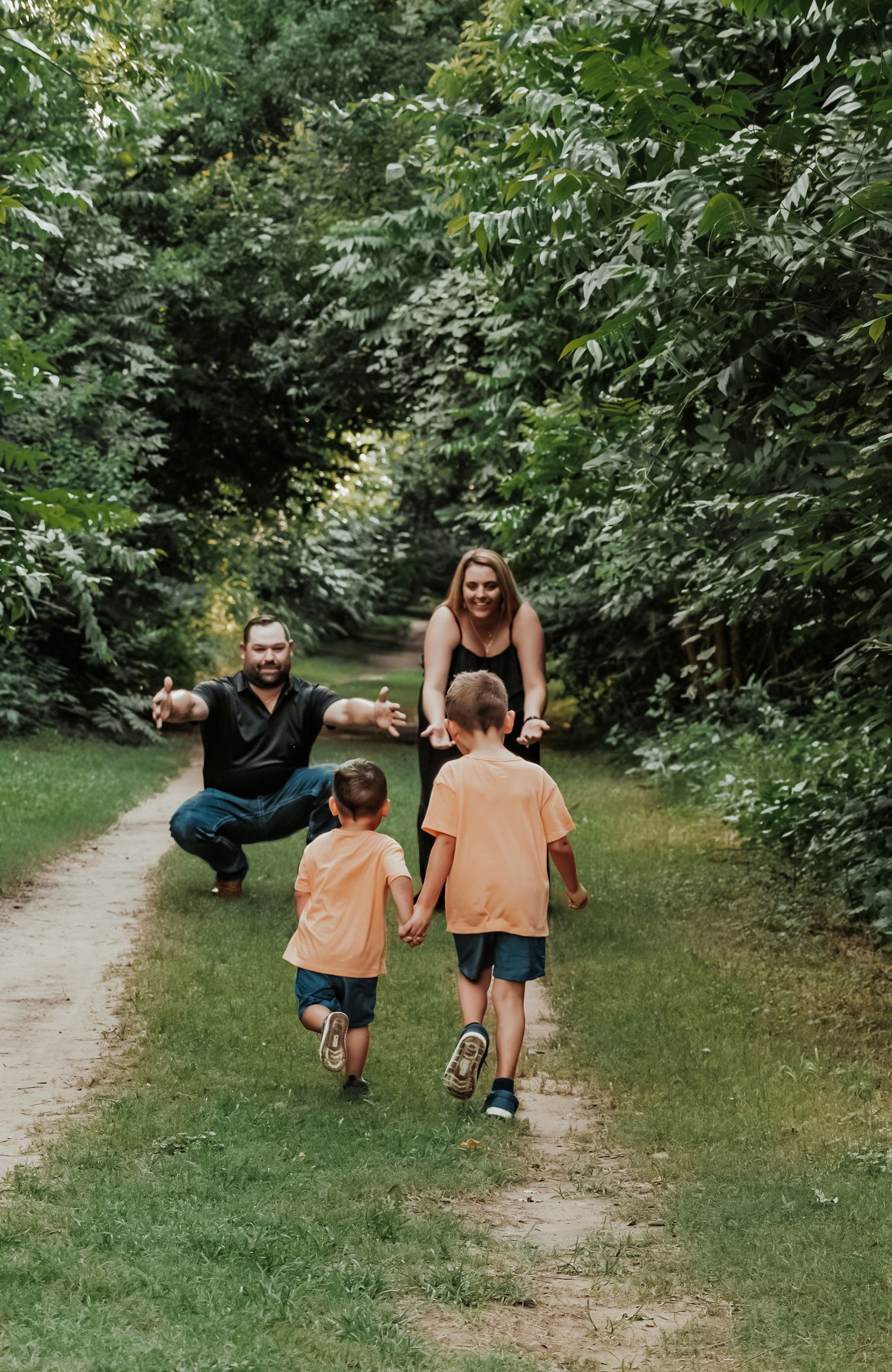Joyful family running toward parents with open arms on a green park path.