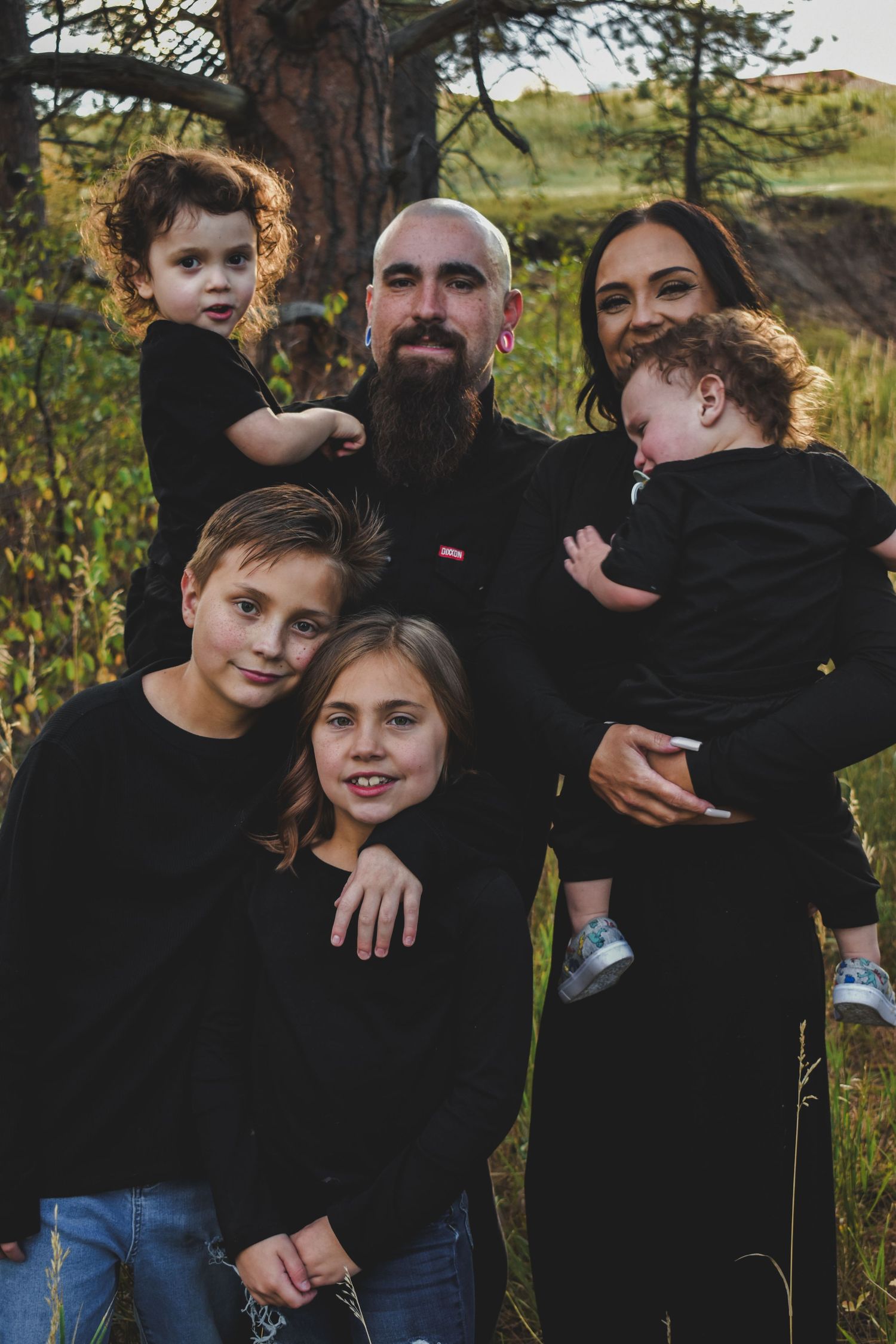 Family of six in matching black outfits posing outdoors in a scenic nature setting.