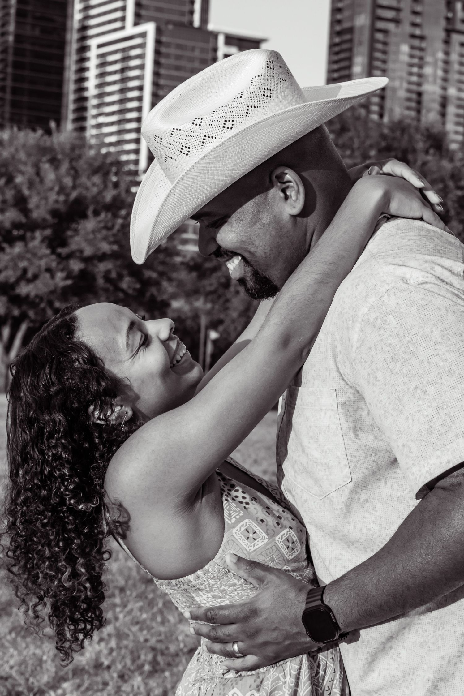 Black and white photo of a couple in a loving embrace with a city skyline behind them.