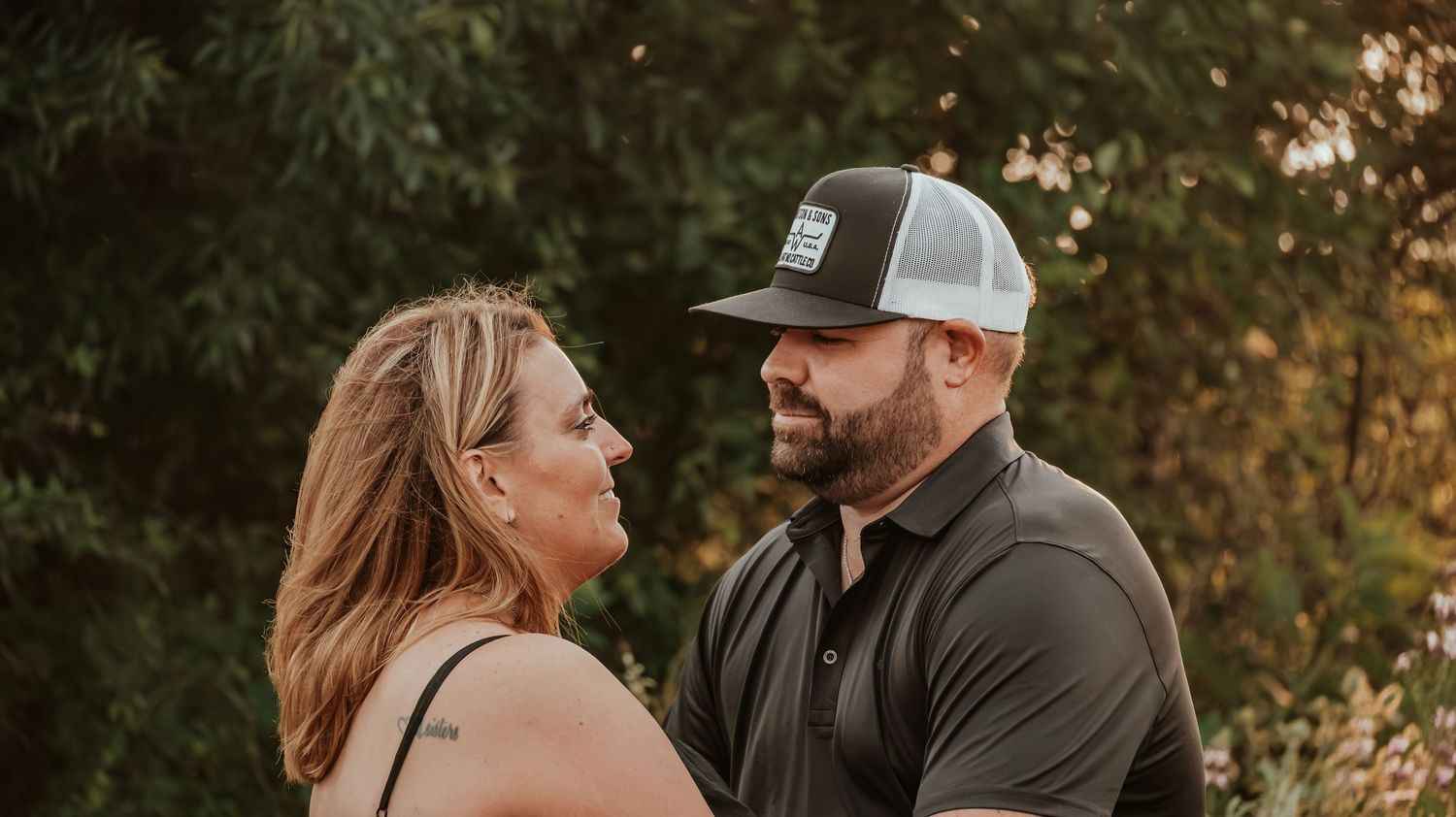 A couple shares a romantic outdoor moment, against lush green trees.
