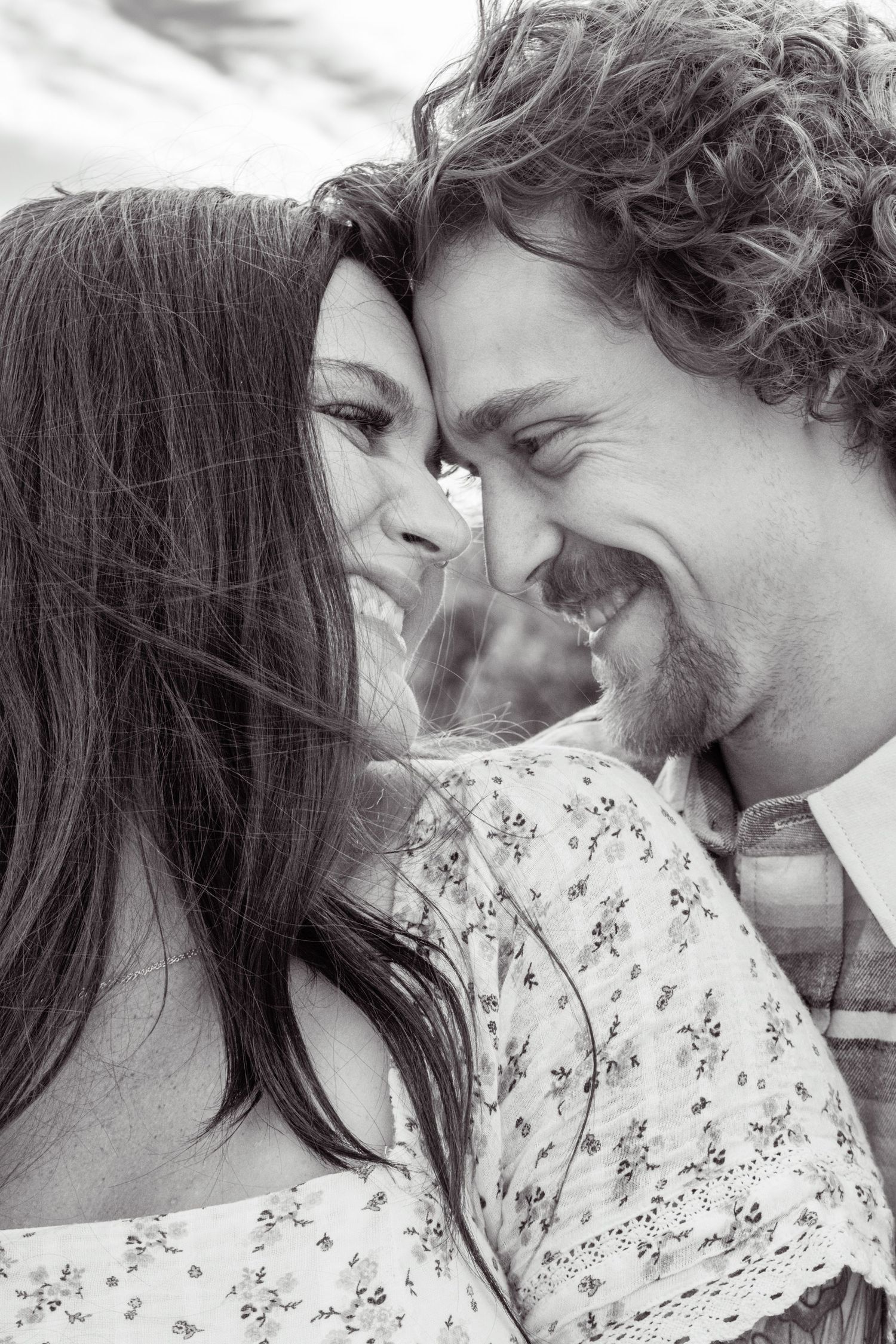 A black and white close-up of a laughing couple touching foreheads in a romantic outdoor moment.