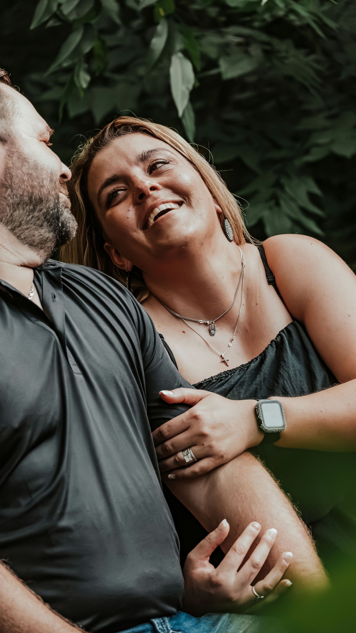 Joyful couple embracing in a lush garden, woman laughing as man whispers in her ear.