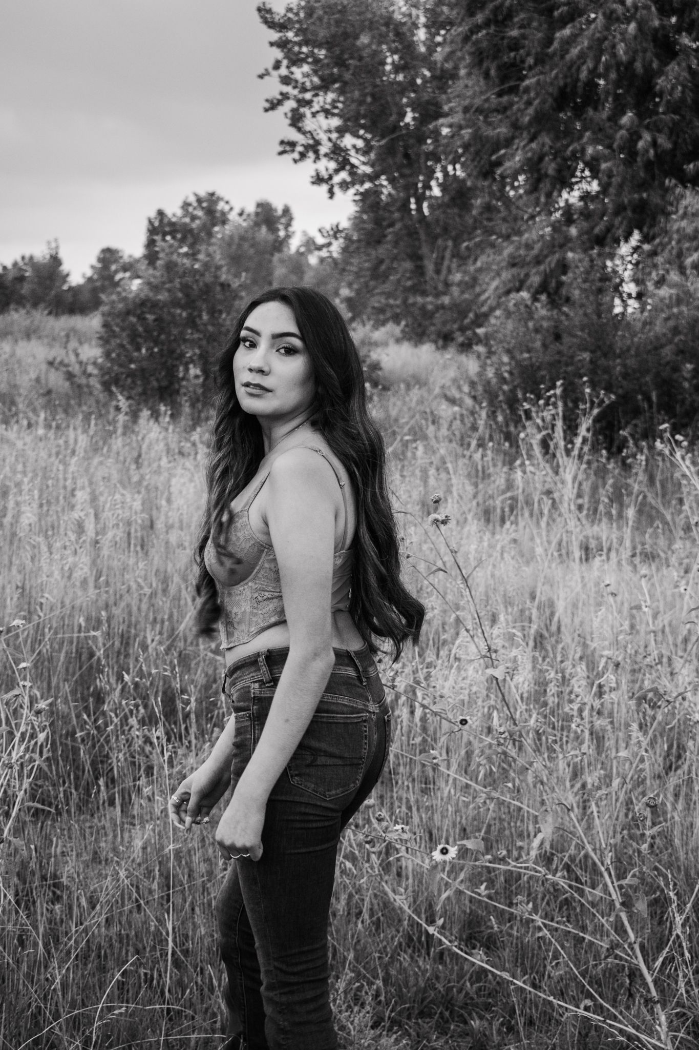 Young woman with long dark hair poses in a field of tall grass, black and white outdoor portrait photography for senior photos.