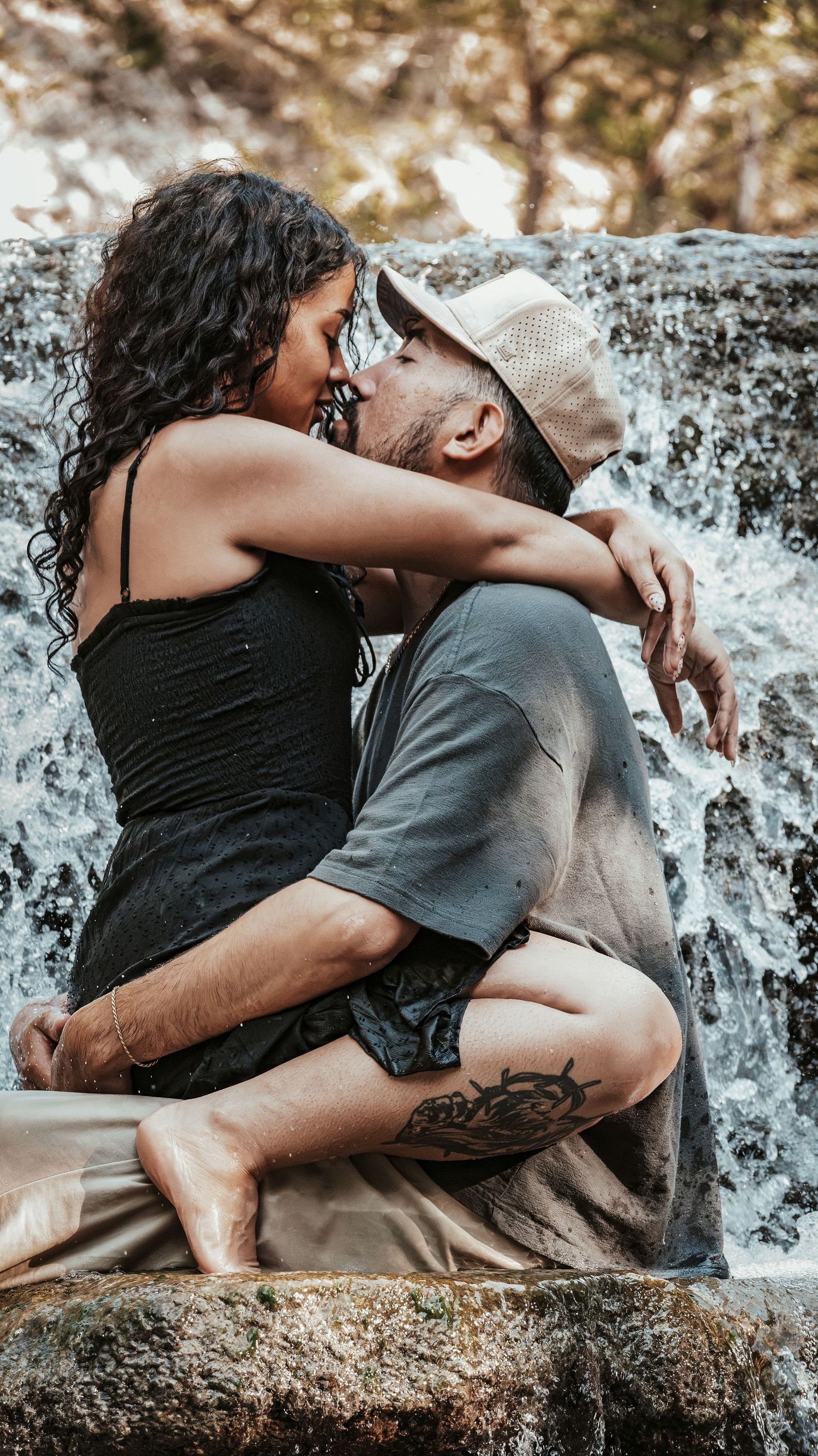 Couple embracing and kissing on wet rocks with a cascading waterfall in the background.