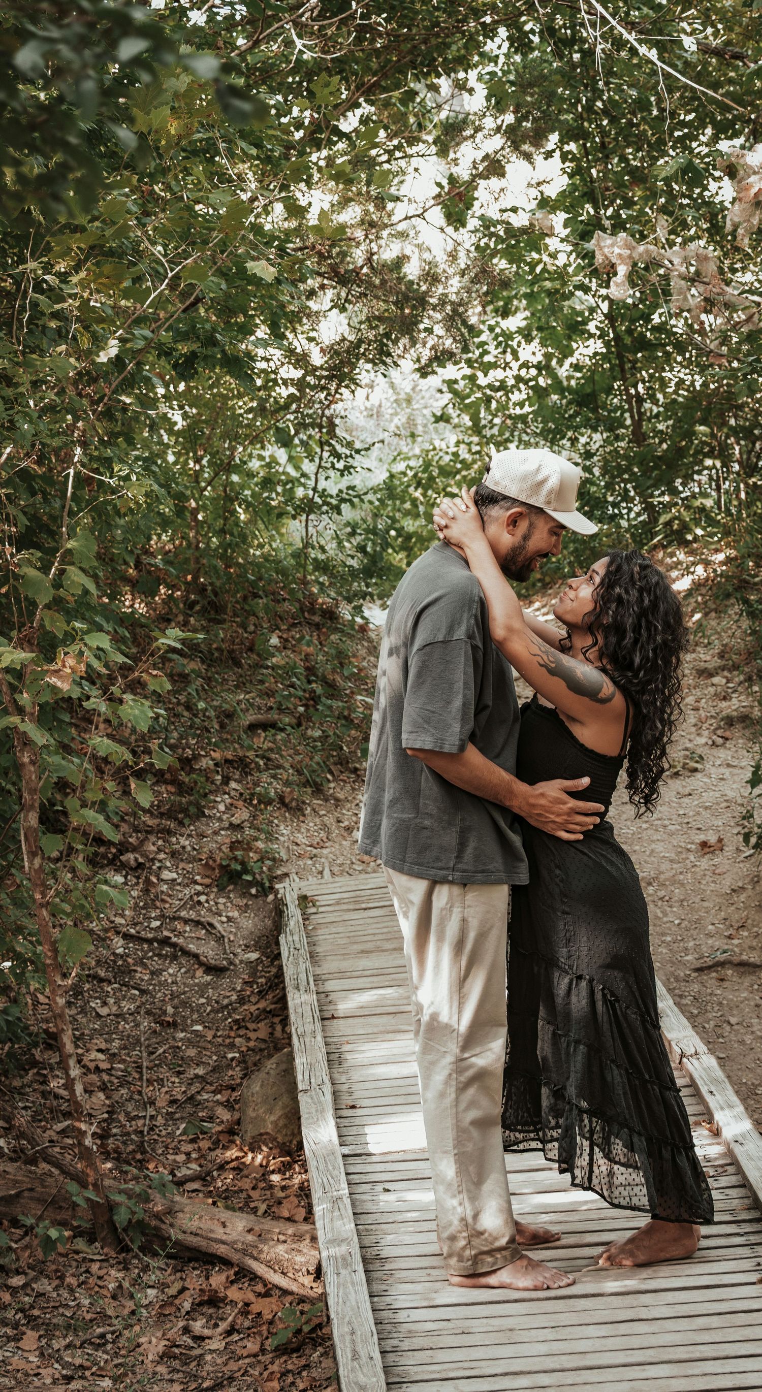 Couple sharing a romantic moment on a wooden boardwalk path surrounded by lush green trees for a couples session.