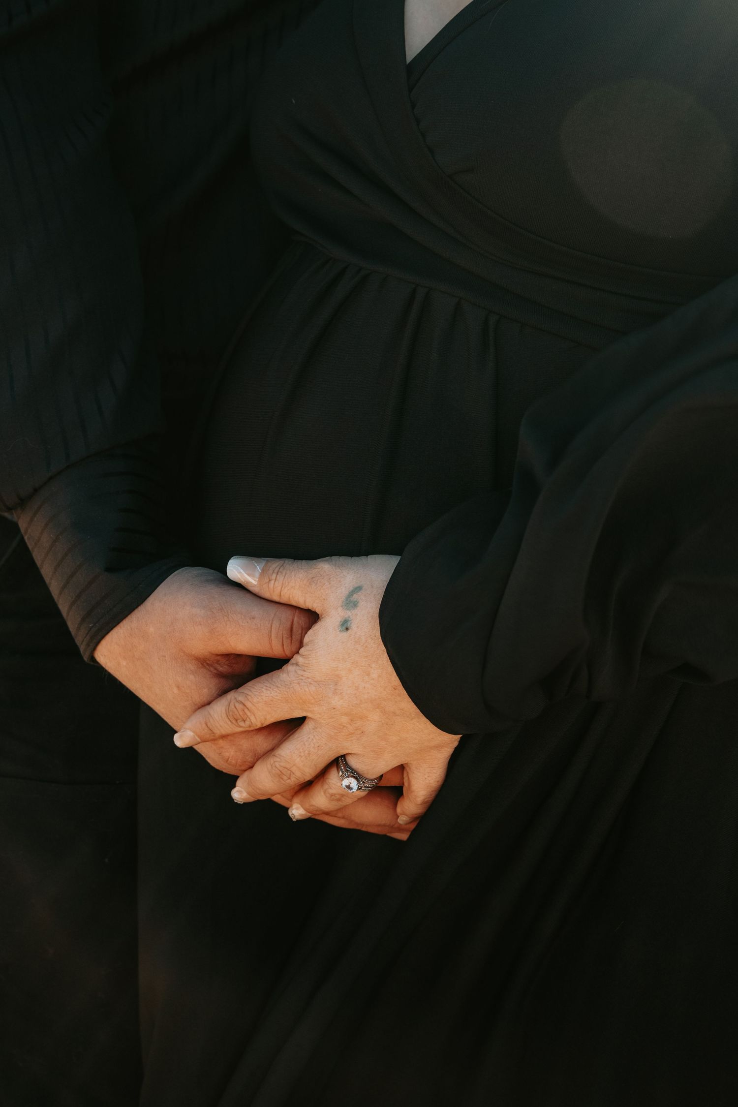 Close-up of couple holding hands over pregnant belly, woman wearing a black dress and diamond ring.