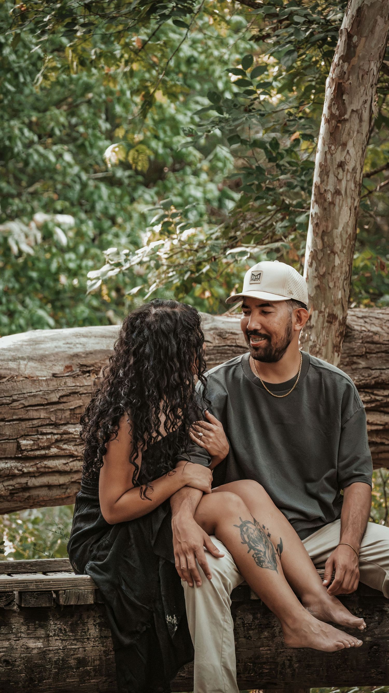 Couple sitting on a fallen log in a forest, smiling at each other for a couples session.