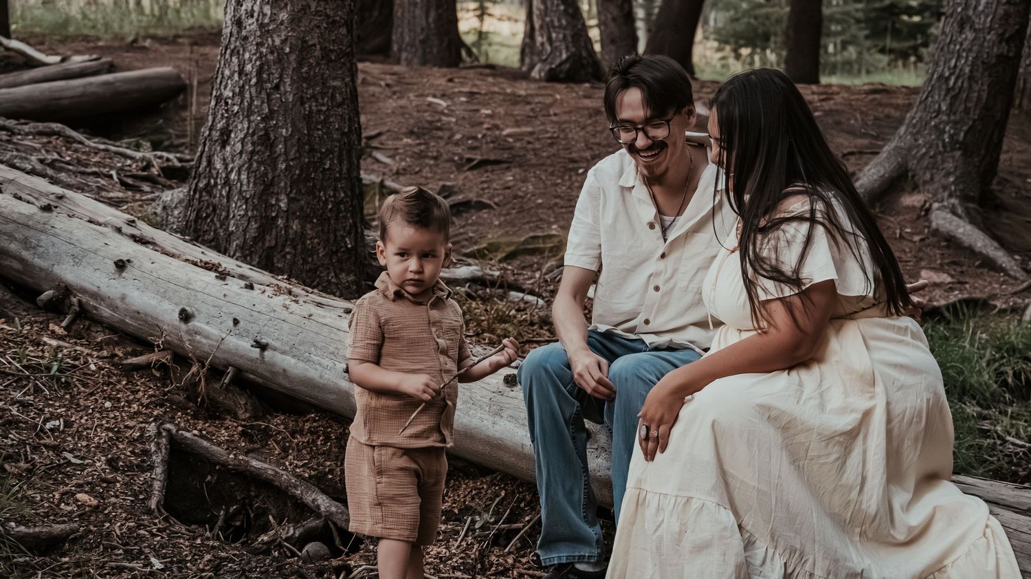 A young family with a toddler boy enjoys a peaceful moment together among fallen logs in a forest.