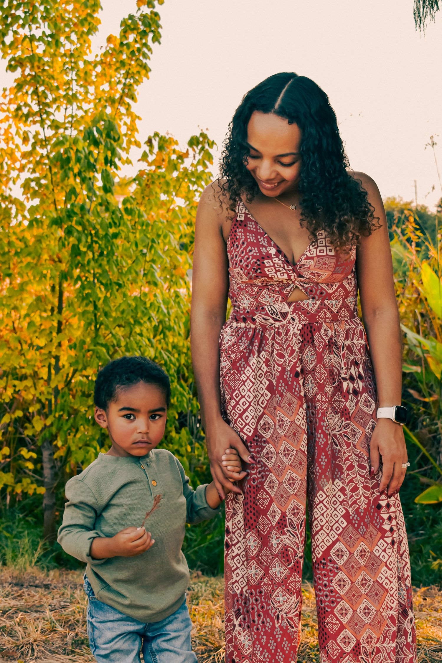 A mother hands with her toddler son outdoors among autumn foliage for a family session.