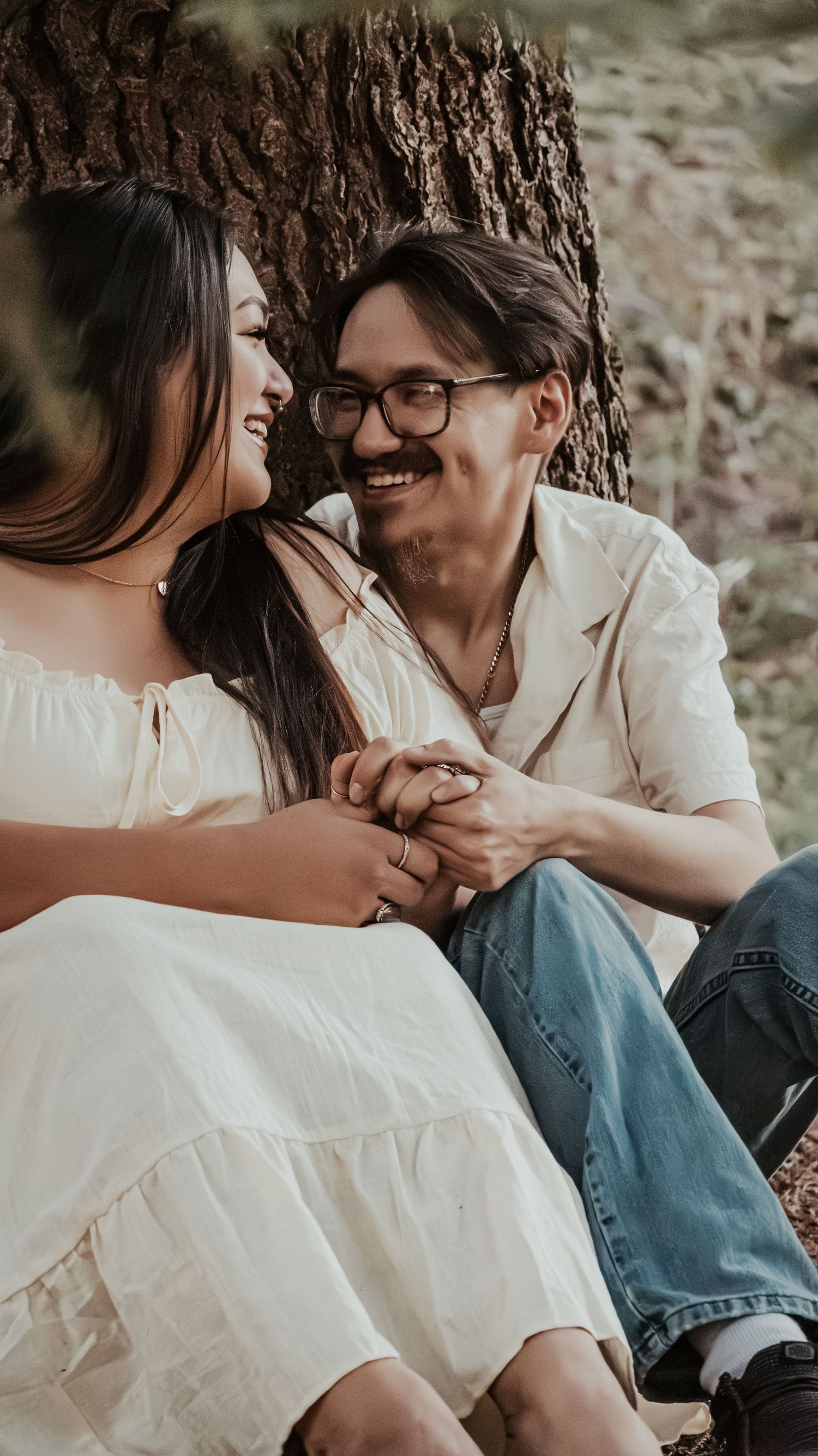 Happy couple laughing and holding hands while leaning against a tree.