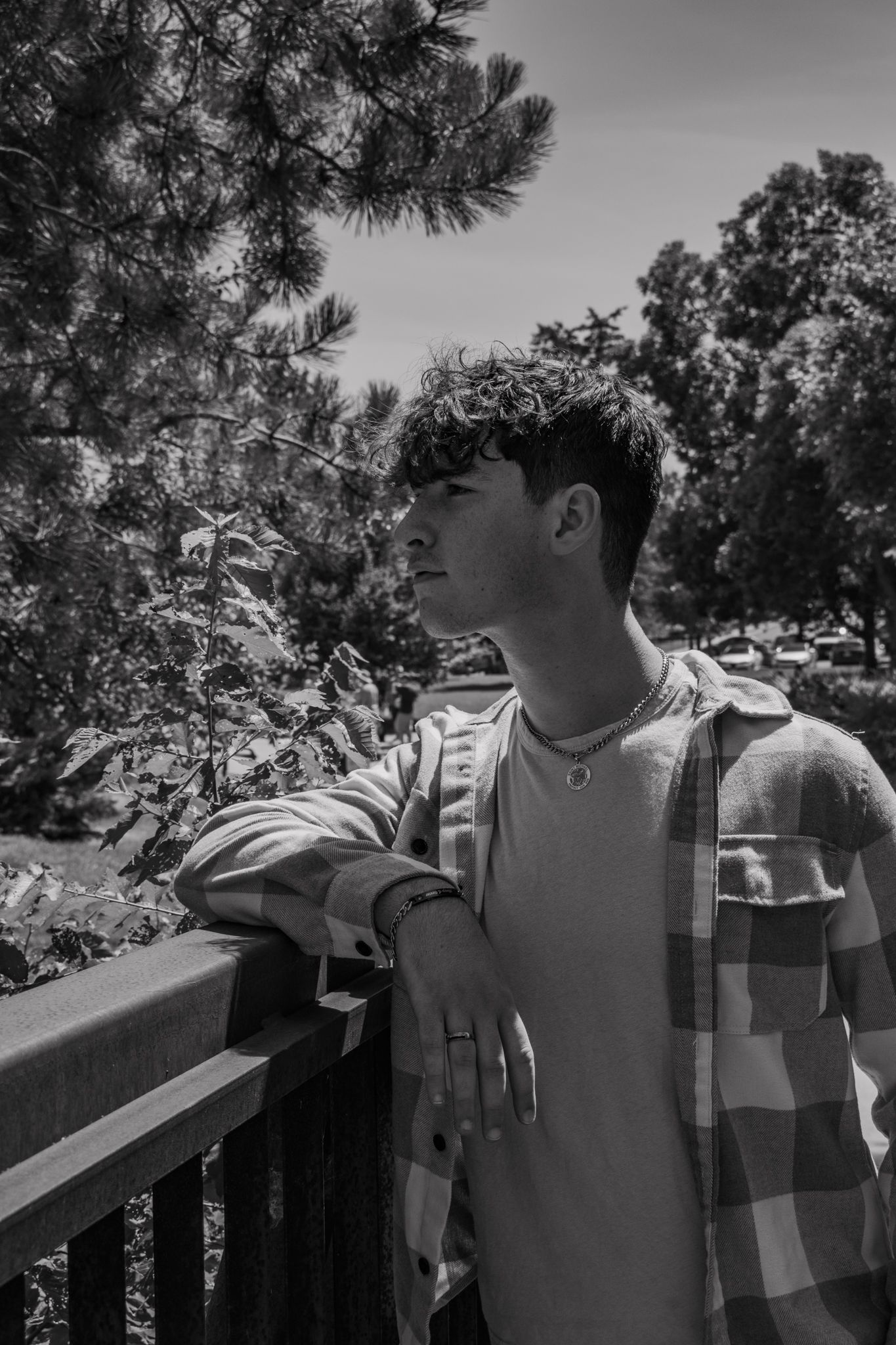 Young man in plaid shirt leaning on wooden railing outdoors in black and white portrait photo for senior photos.