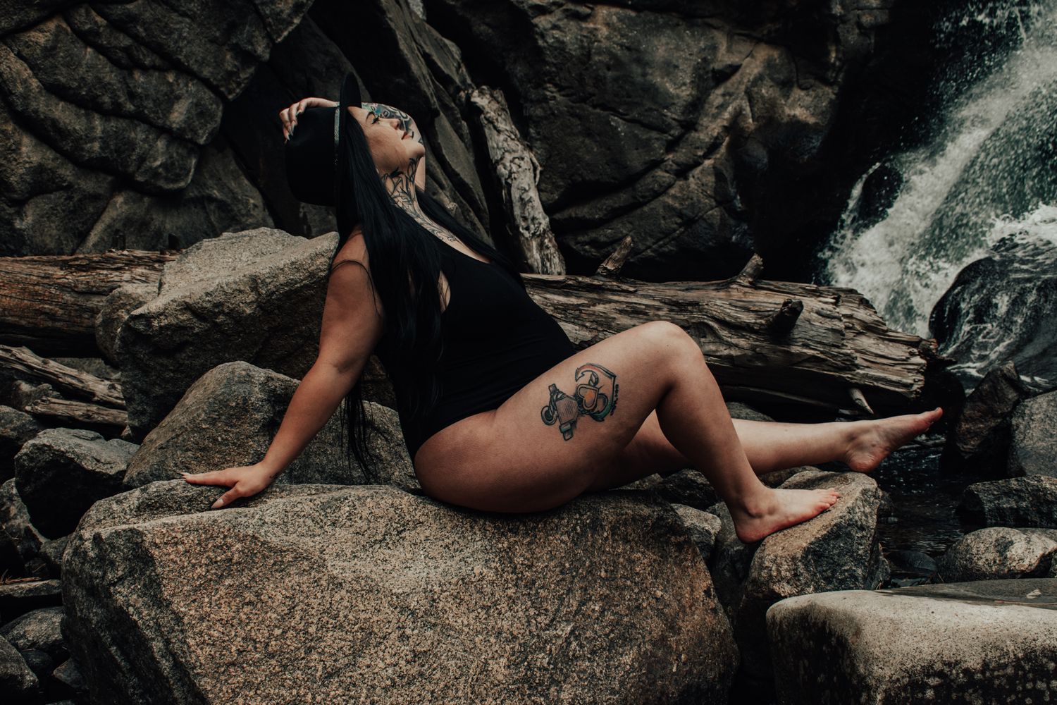 A pregnaant woman in black swimsuit posing on rocks near a waterfall. Maternity Photographer in Pflugerville, Tx
