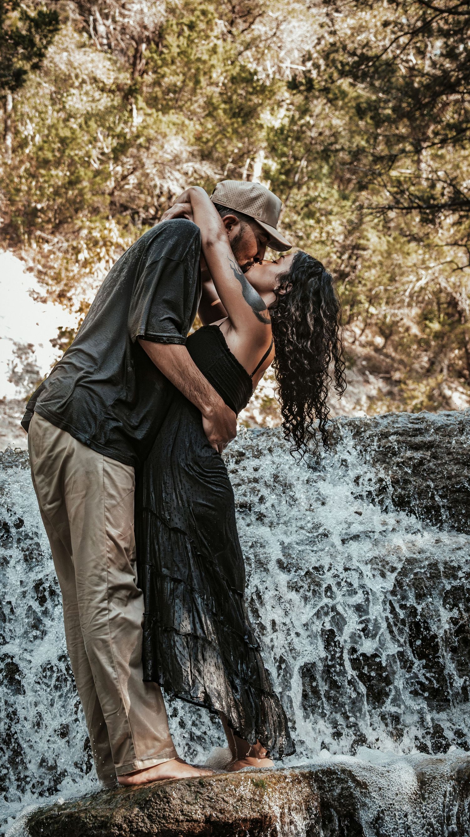 Couple sharing a romantic kiss in front of a cascading waterfall surrounded by lush trees for a couples session.