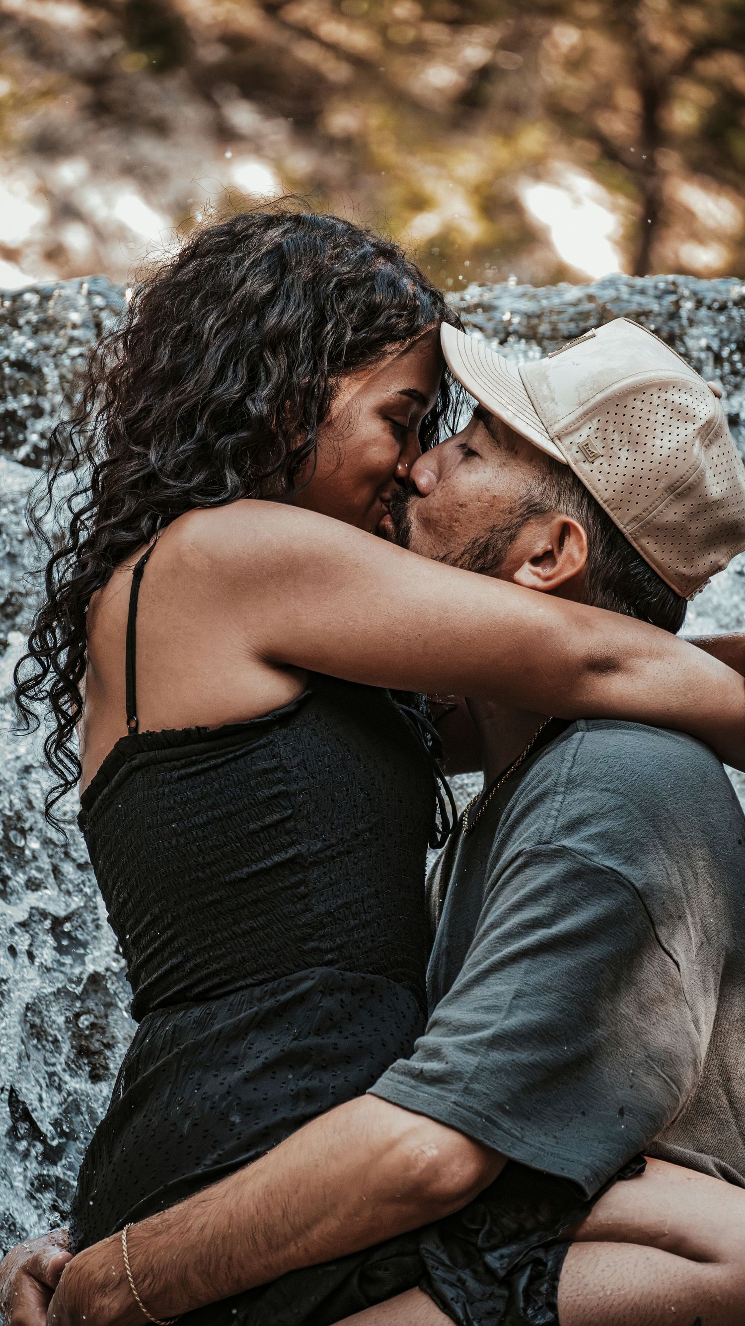 Close-up of a couple sharing a kiss on rocky terrain near a waterfall in nature.