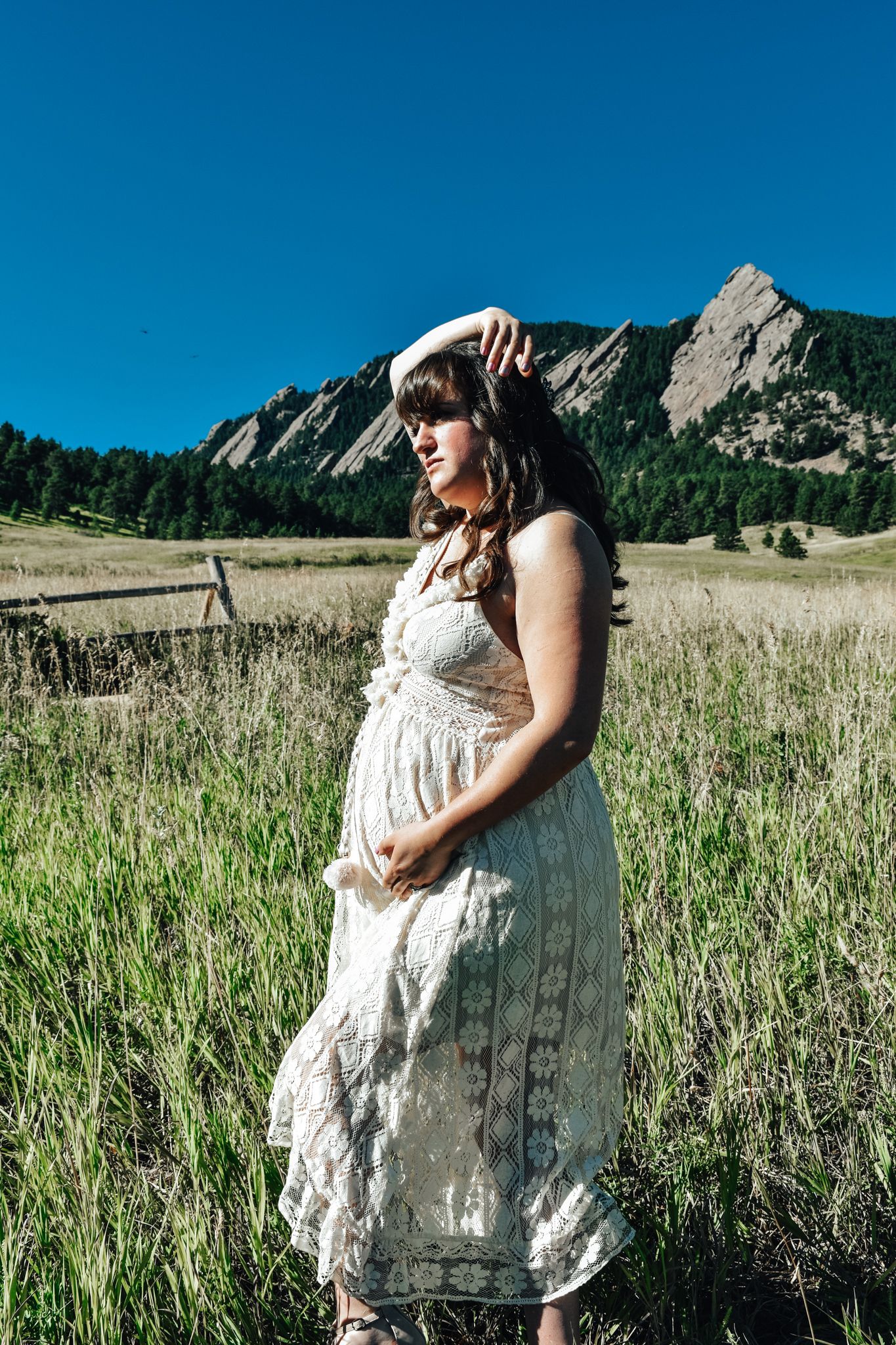 Pregnant woman in white lace dress standing in green meadow.  Maternity Photographer in Pflugerville, Tx