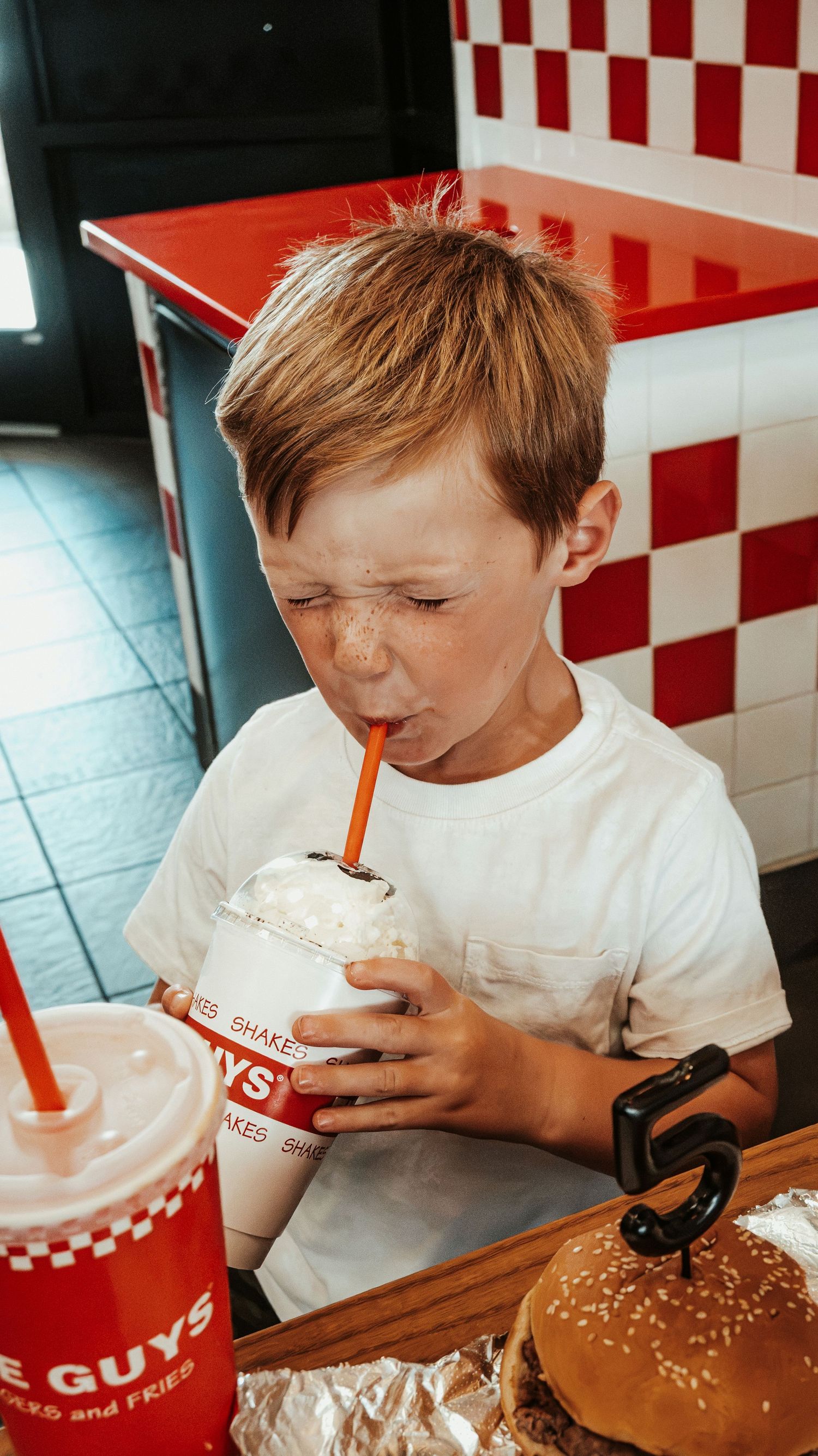 Young boy sipping a milkshake at Five Guys burger restaurant, eyes closed in delight. Family Photographer in Pflugerville, Tx