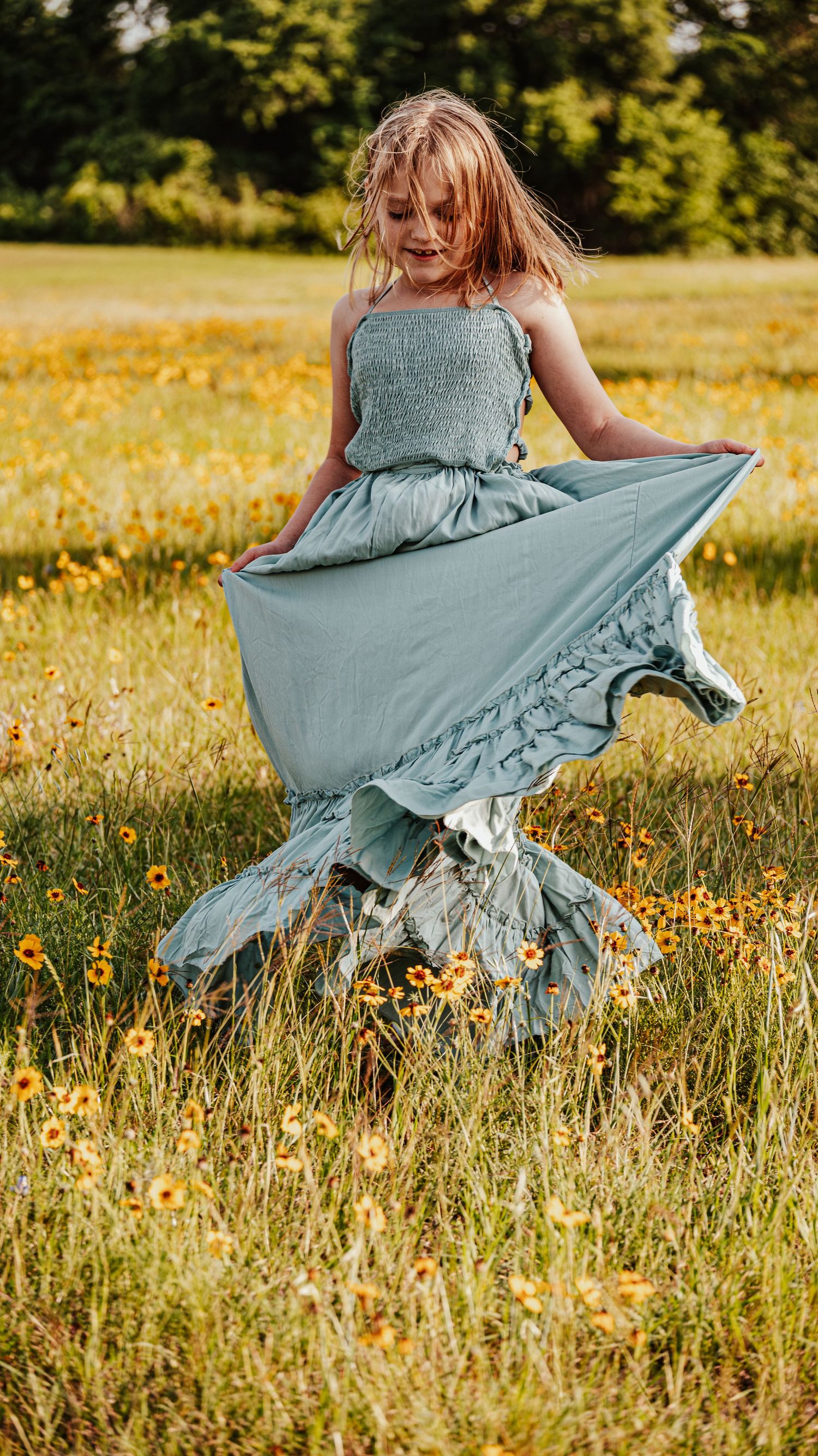 Young girl twirling in sage green maxi dress in wildflower meadow.