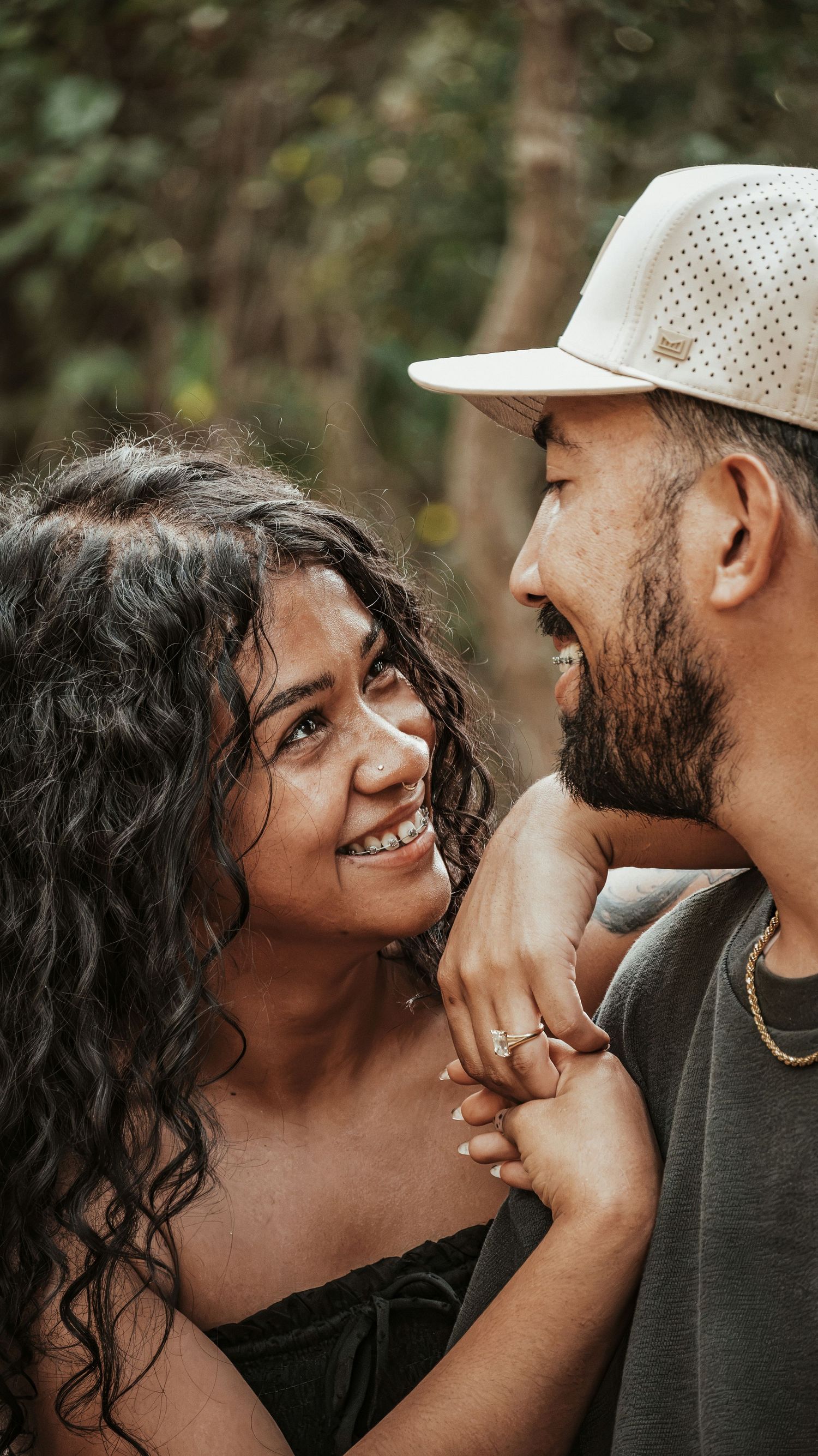 A smiling couple shares a joyful moment outdoors, the woman wearing a ring for a couples session.