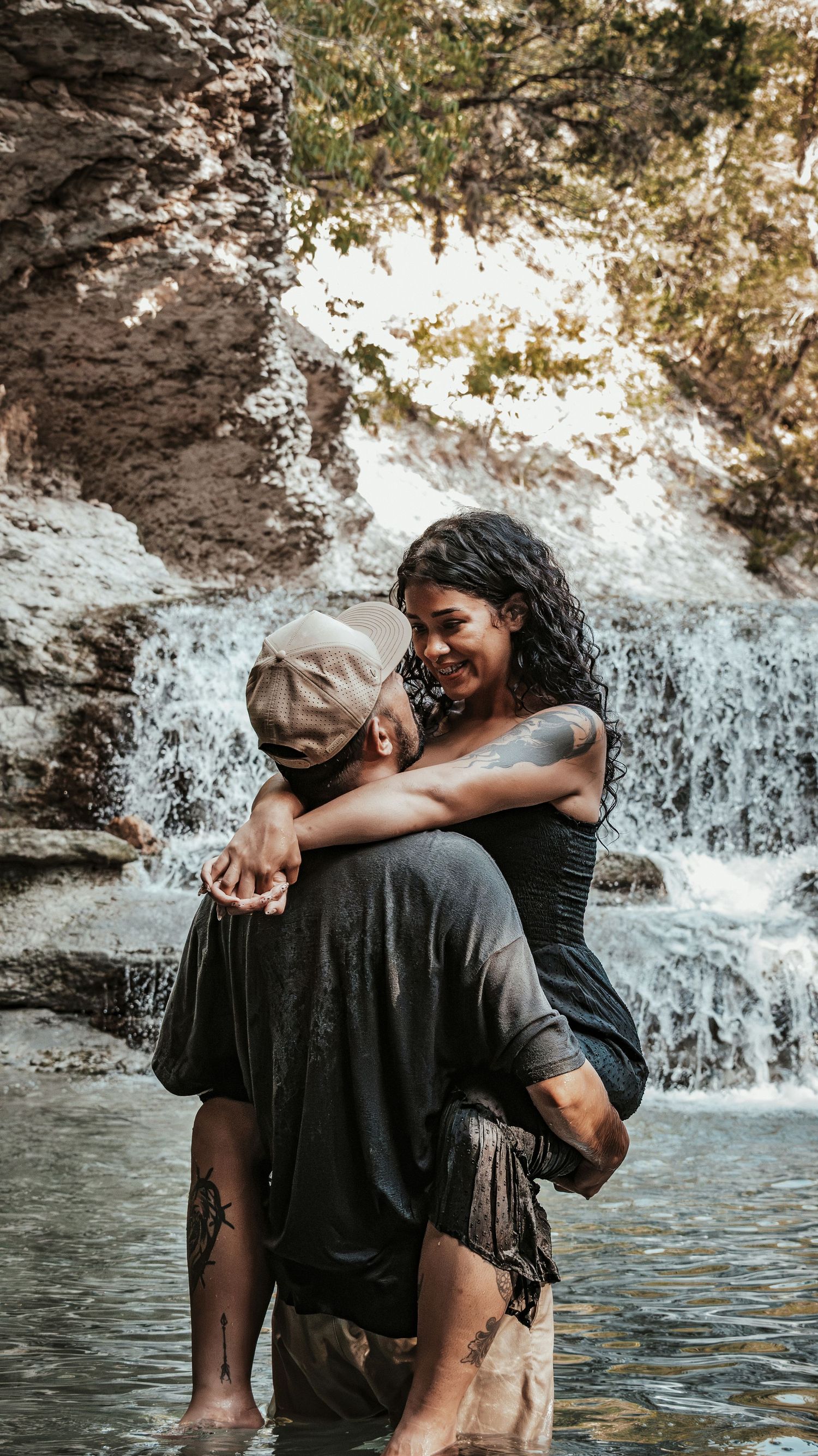 Woman laughing joyfully as man carries her in front of a waterfall.