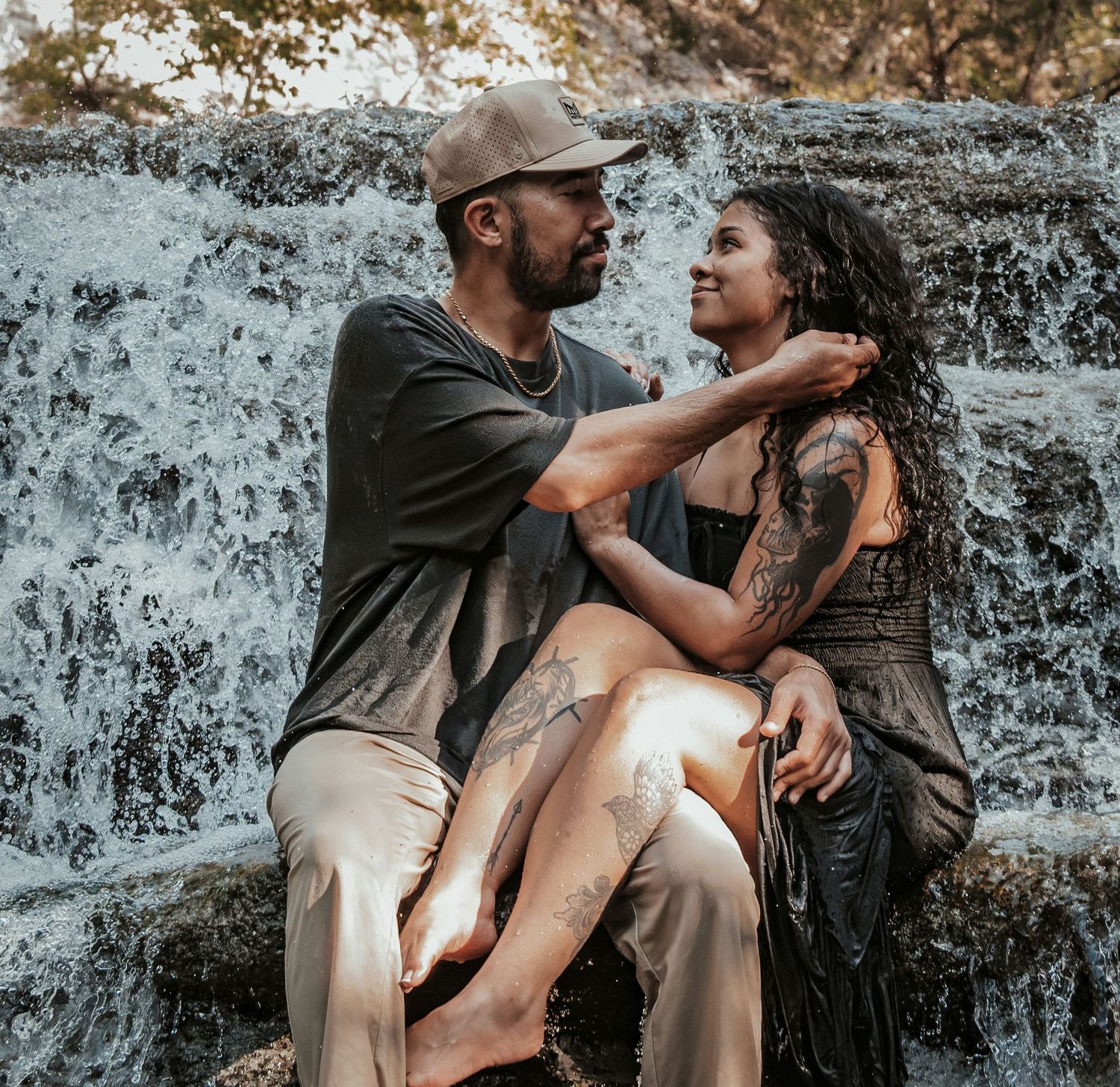 Man tenderly touching womans face while she sits on his lap in front of a flowing waterfall.