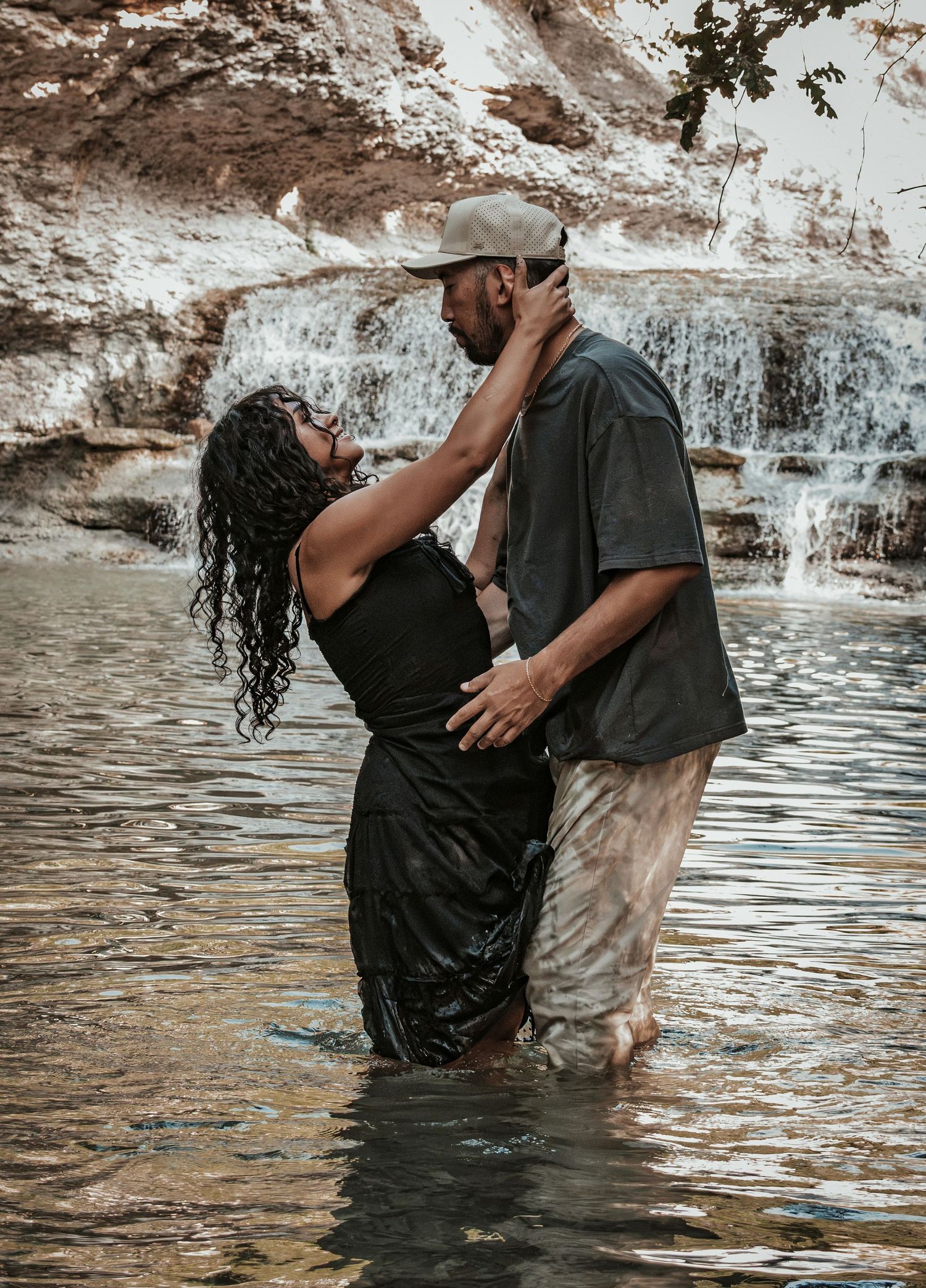 Couple standing in a shallow river embracing romantically with a waterfall for a couples session.