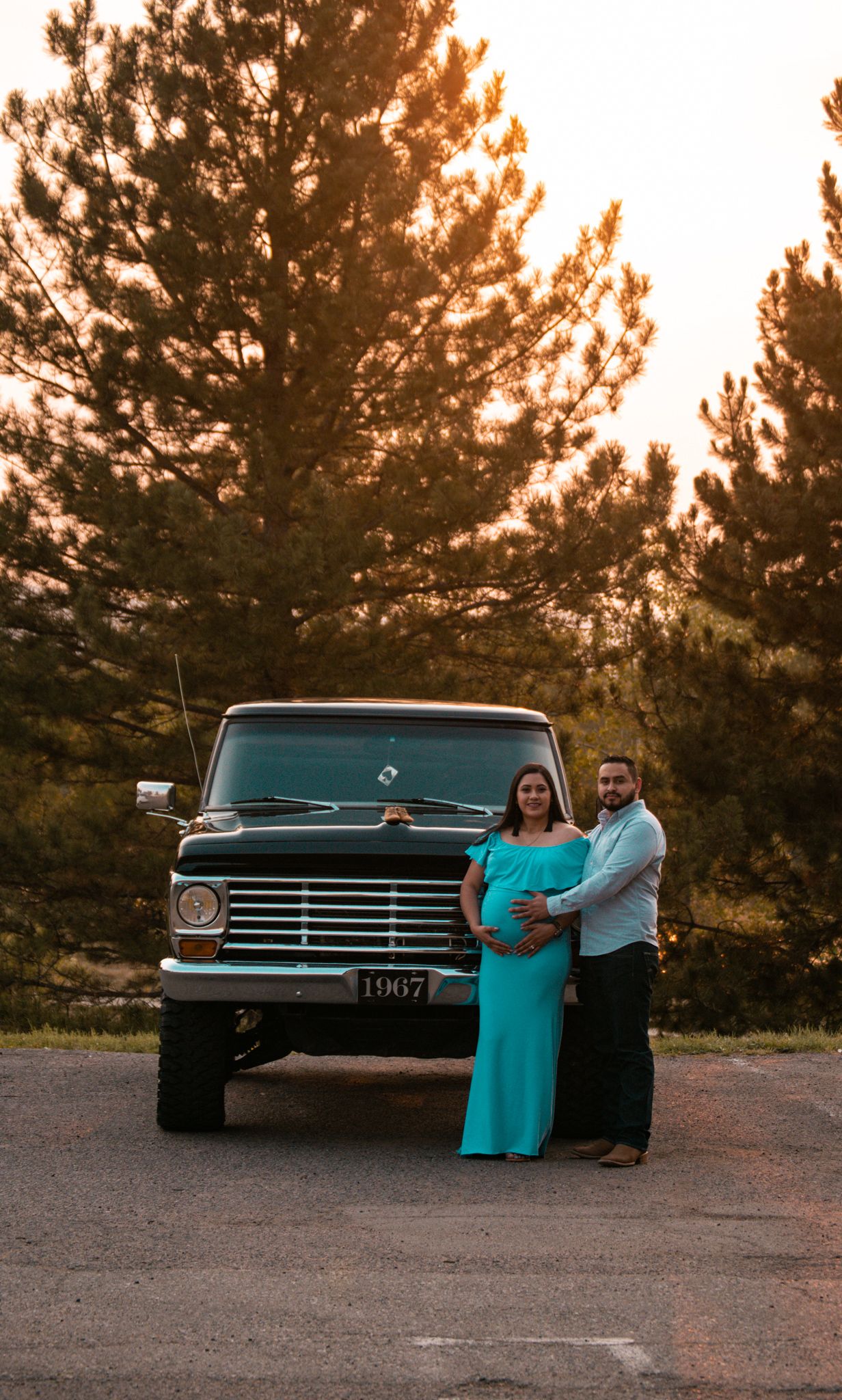 Pregnant couple posing in front of classic 1967 truck at golden sunset.