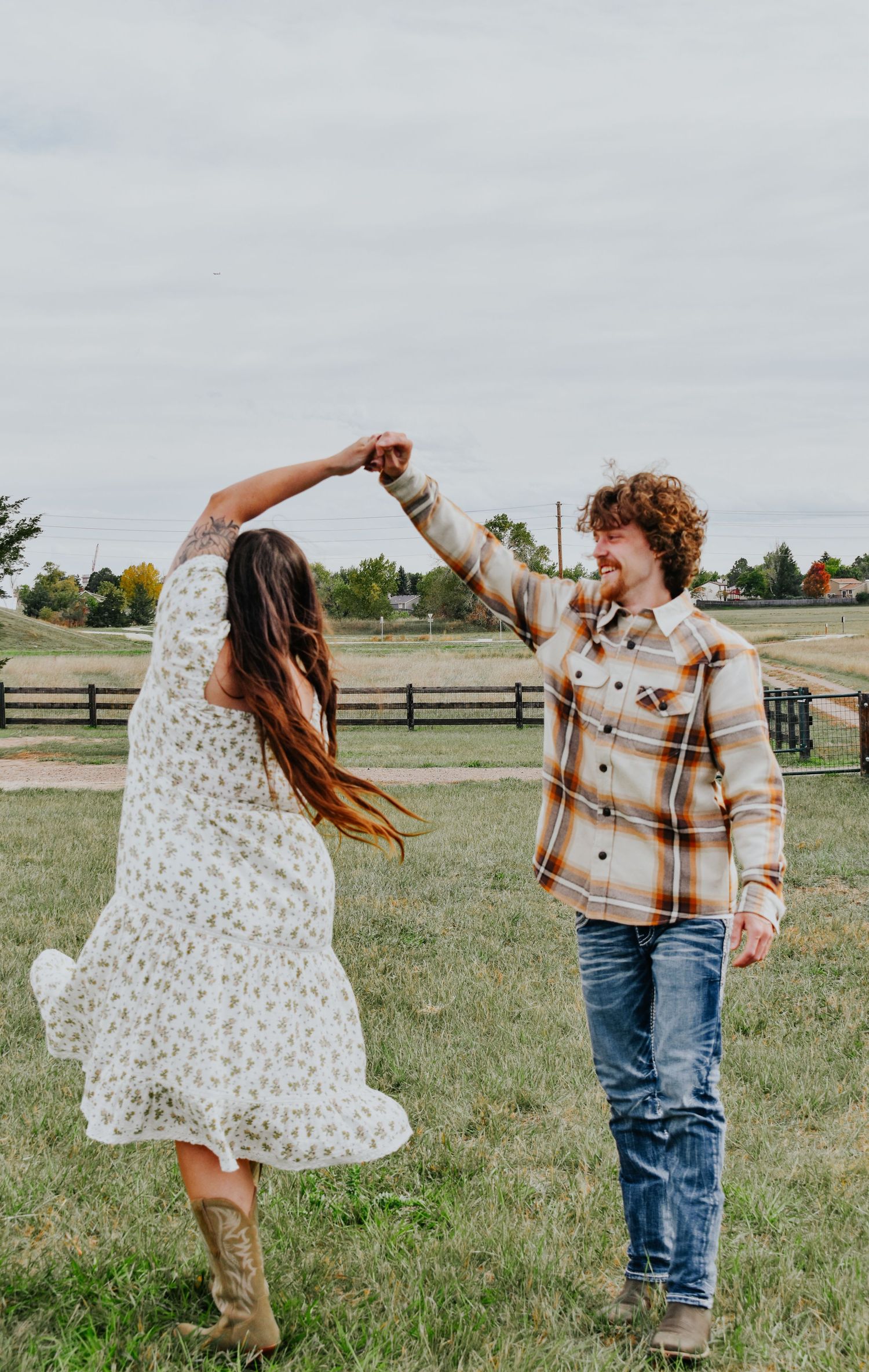Joyful couple dancing in a green farm field, woman in floral dress spinning under mans raised hand.