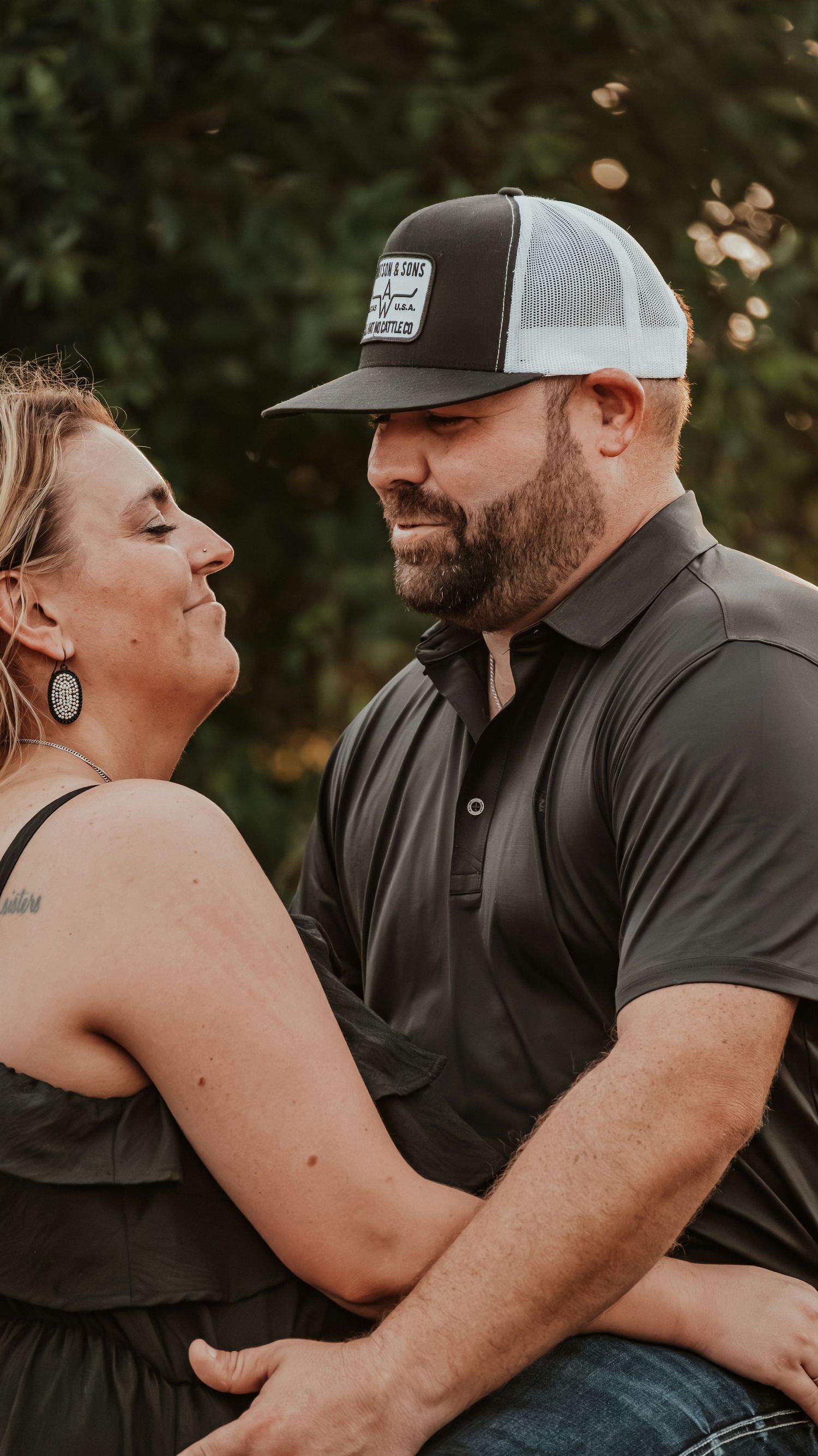 Bearded man in trucker hat smiling at woman during an outdoor couples photo session.