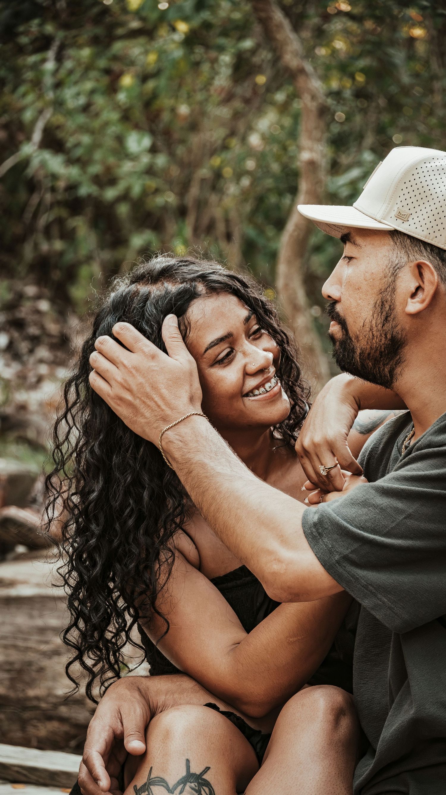 A bearded man in a white cap tenderly holds a smiling woman with curly hair outdoors. Couples Photographer in Pflugerville, Tx