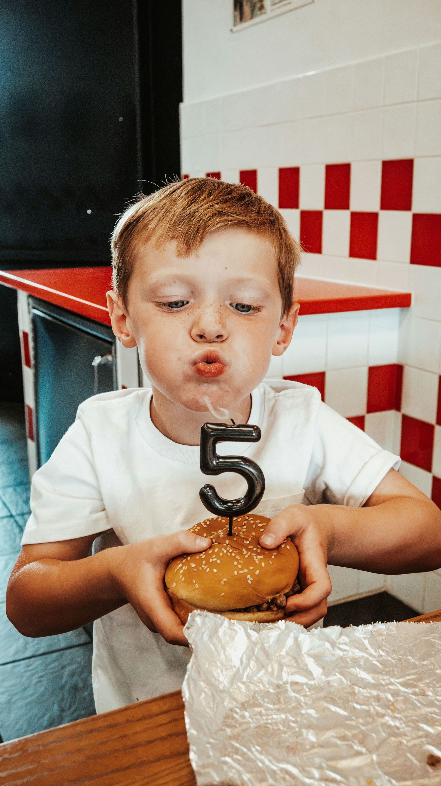 Boy blowing out a number 5 candle on a burger at Five Guys restaurant, celebrating his 5th birthday. Family Photographer in Pflugerville, Tx