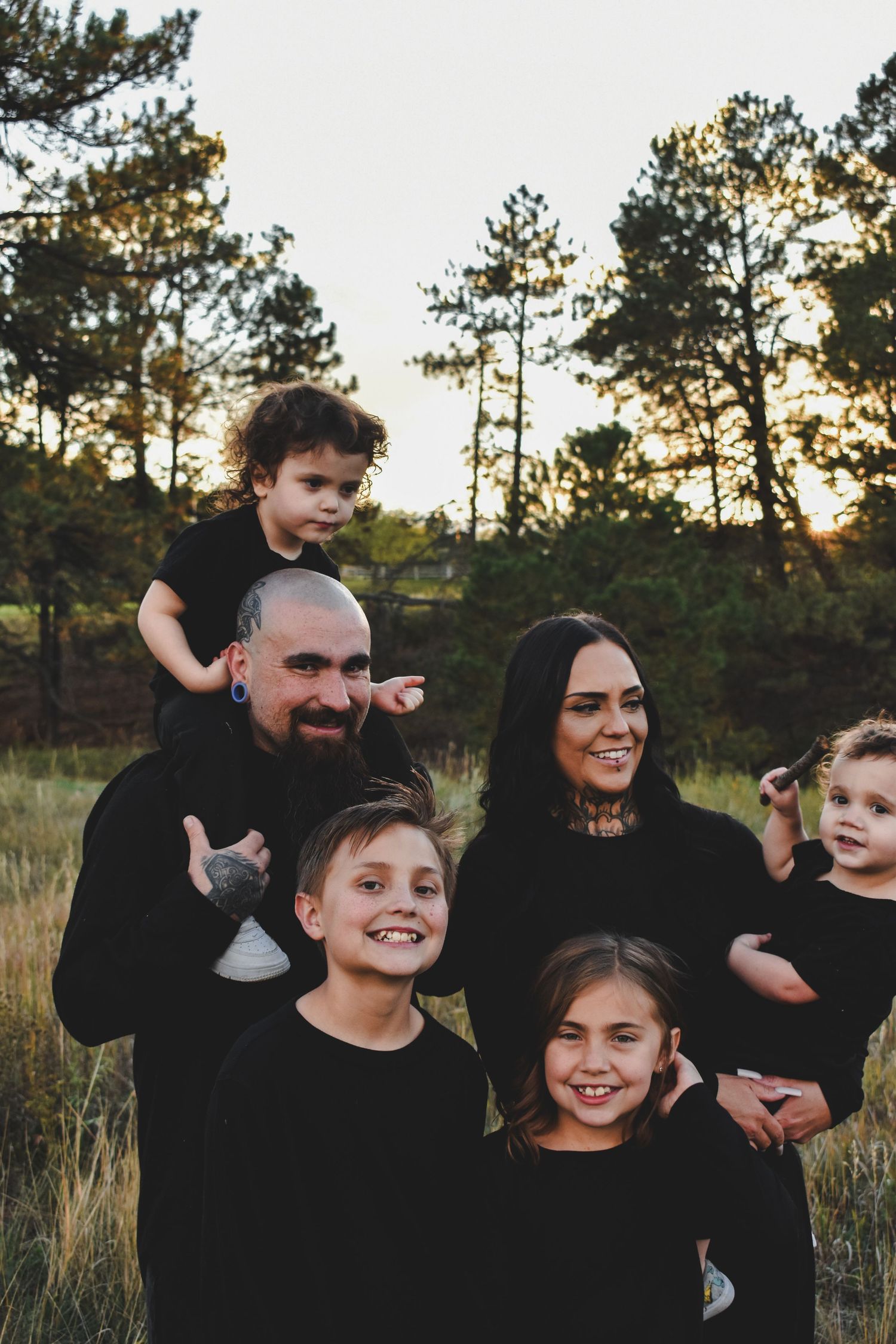 Family of six dressed in black posing together at golden hour in a pine forest.