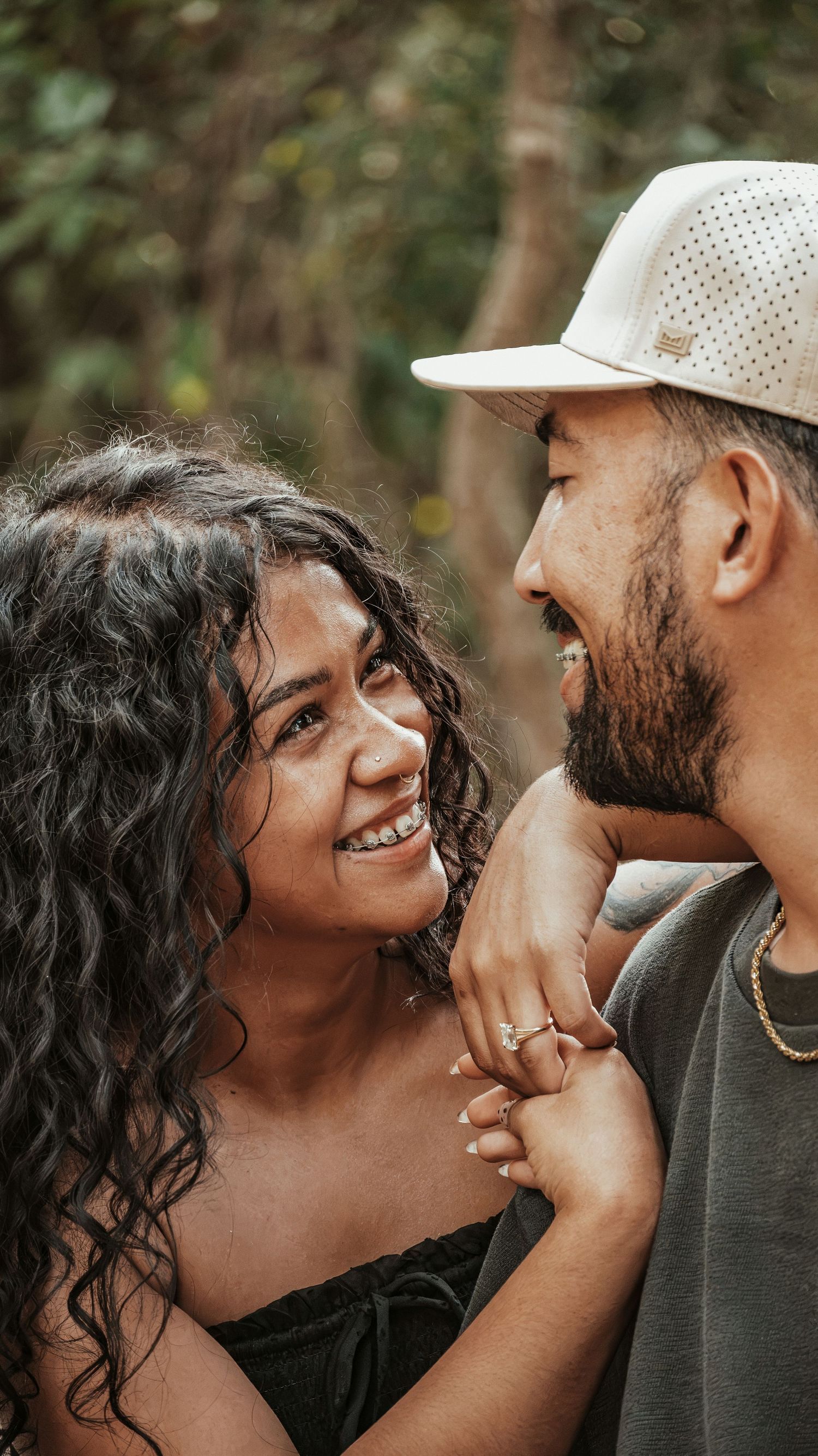 A happy couple laughs together while holding hands outdoors in a wooded setting.