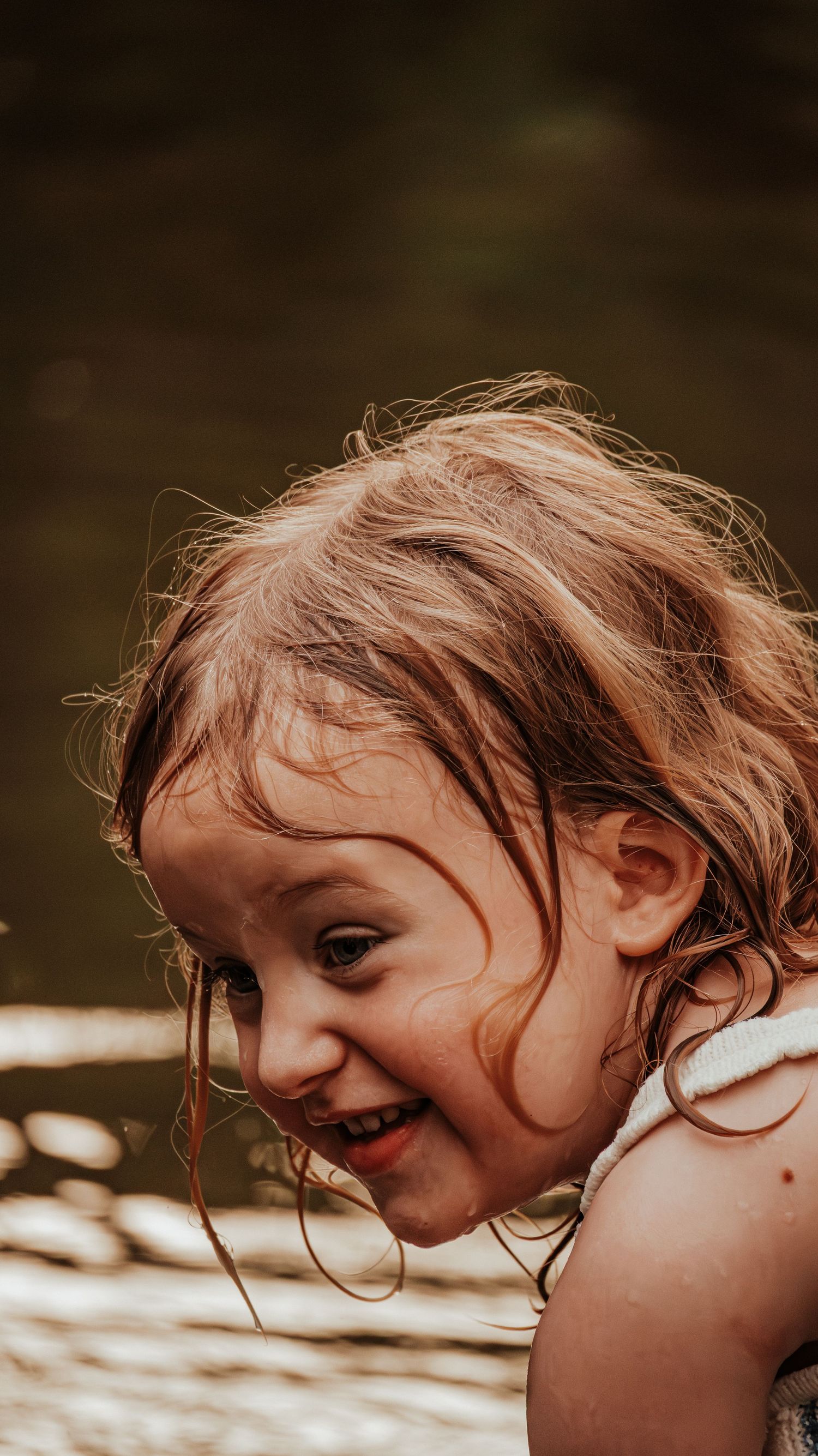 Happy young girl with wet hair smiling outdoors near water.