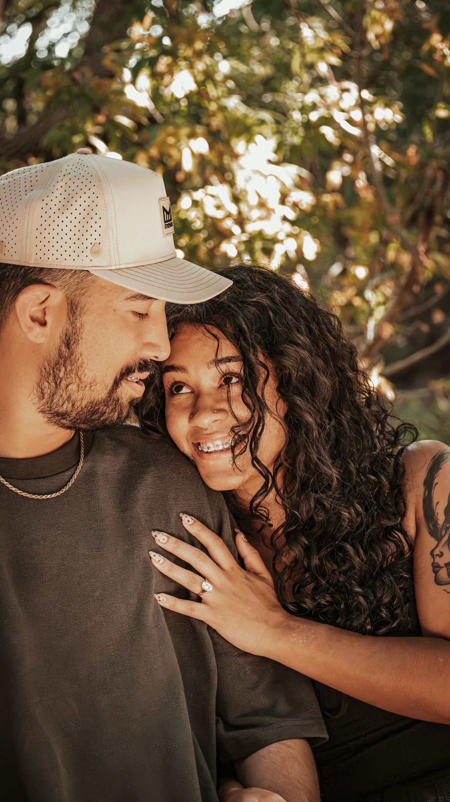 A smiling couple shares a romantic moment outdoors, engagement ring displayed on mans arm for a couples session.