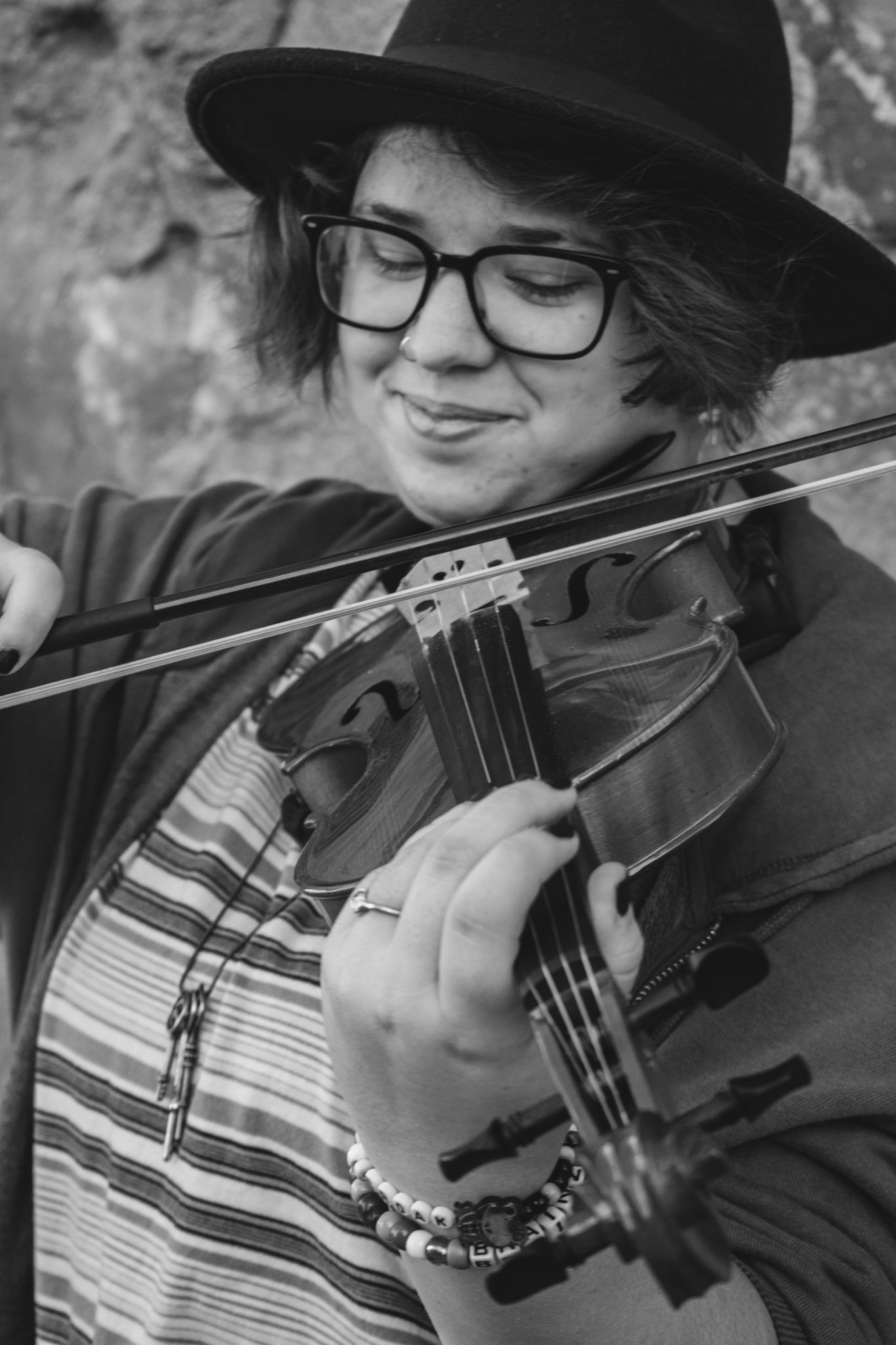 Black and white close-up of young violinist wearing hat and glasses playing instrument outdoors for senior photos.