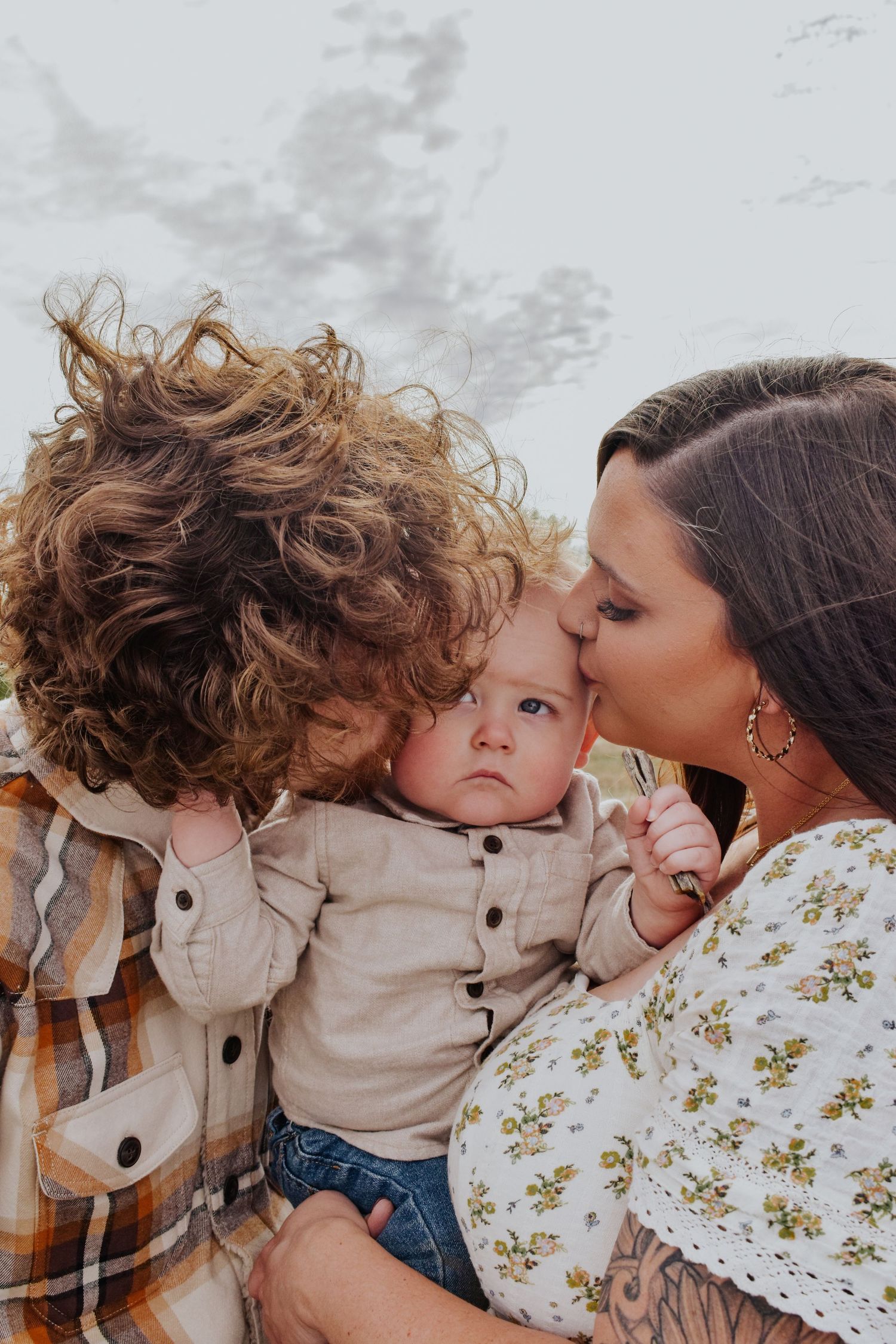 Parents kissing their baby on the cheeks in a sweet outdoor family portrait.