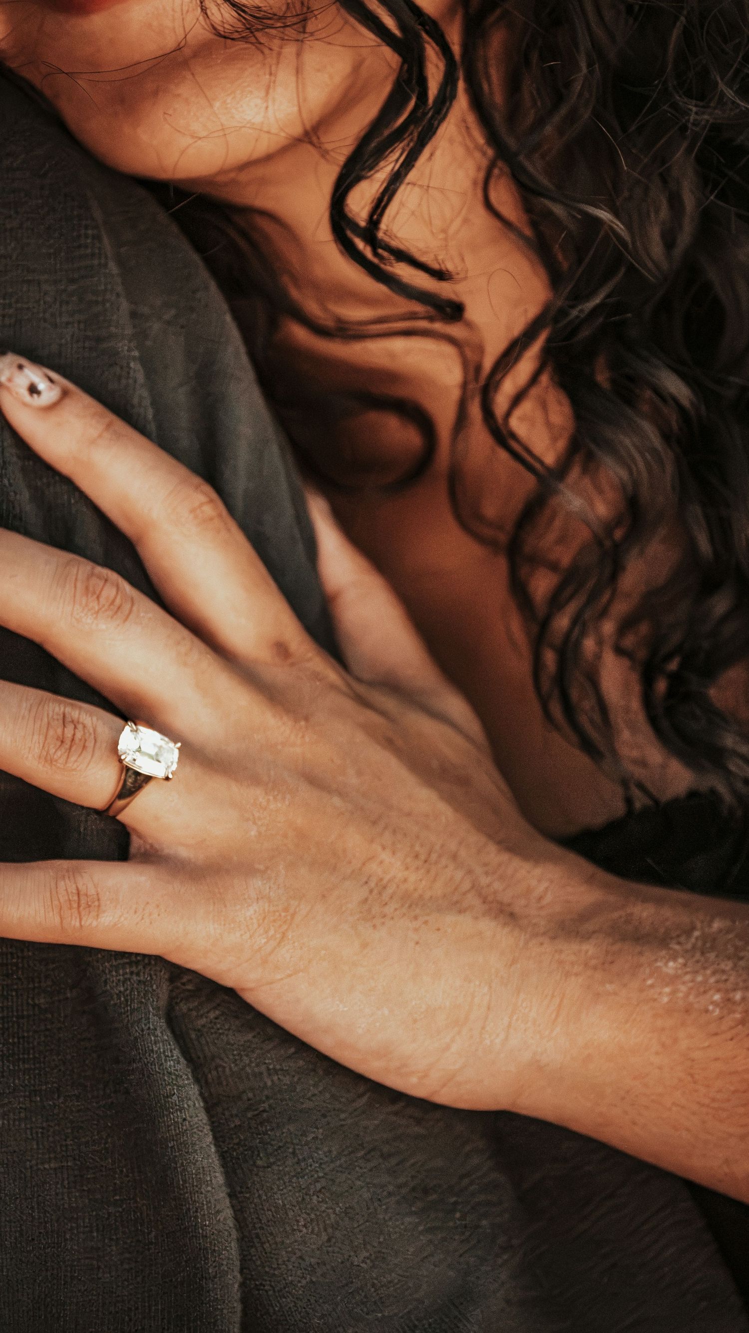 Close-up of a woman's hand with an elegant diamond engagement ring resting on a man's chest for a couples session.