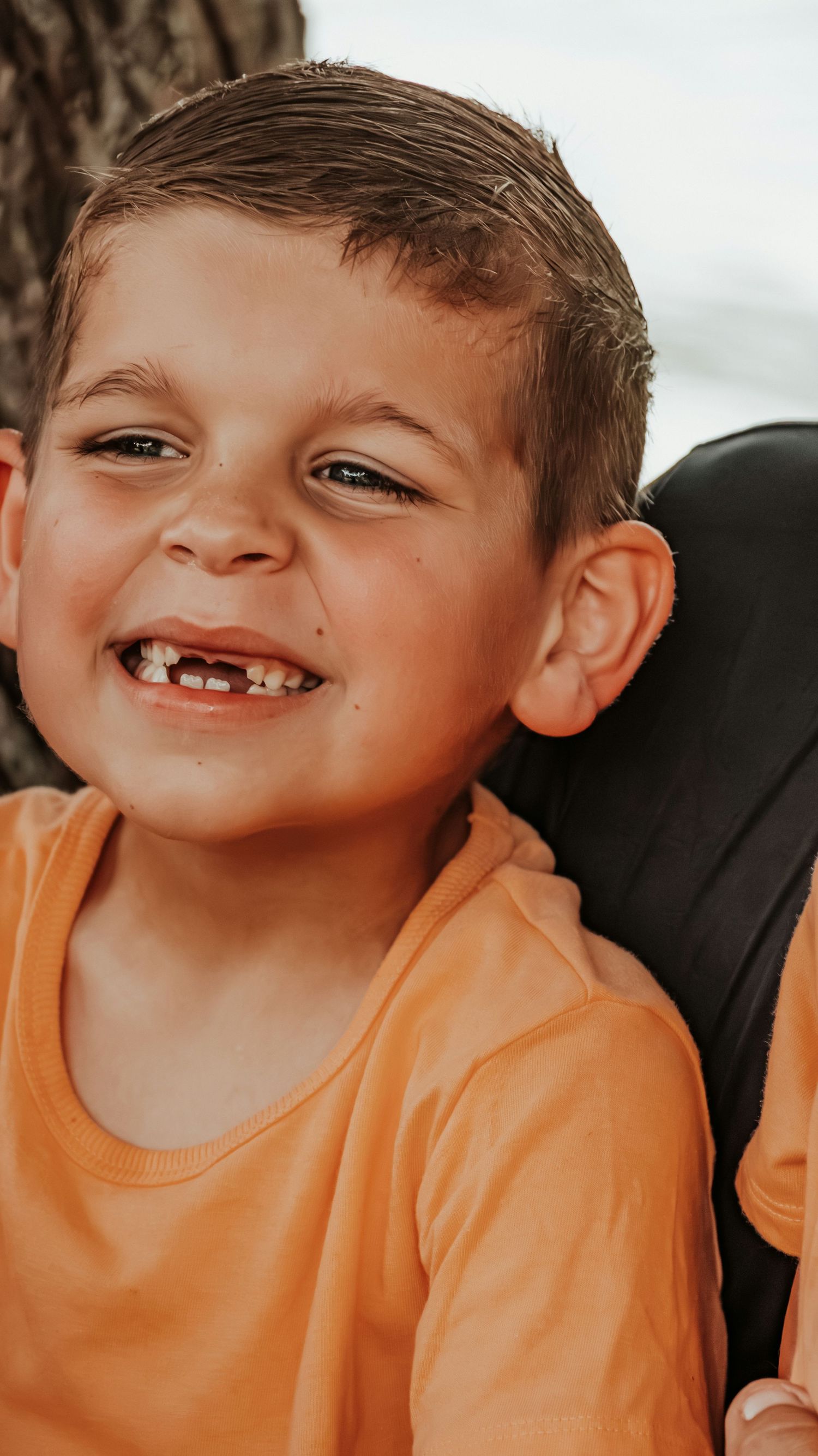 Smiling young boy with missing front teeth wearing an orange shirt outdoors.