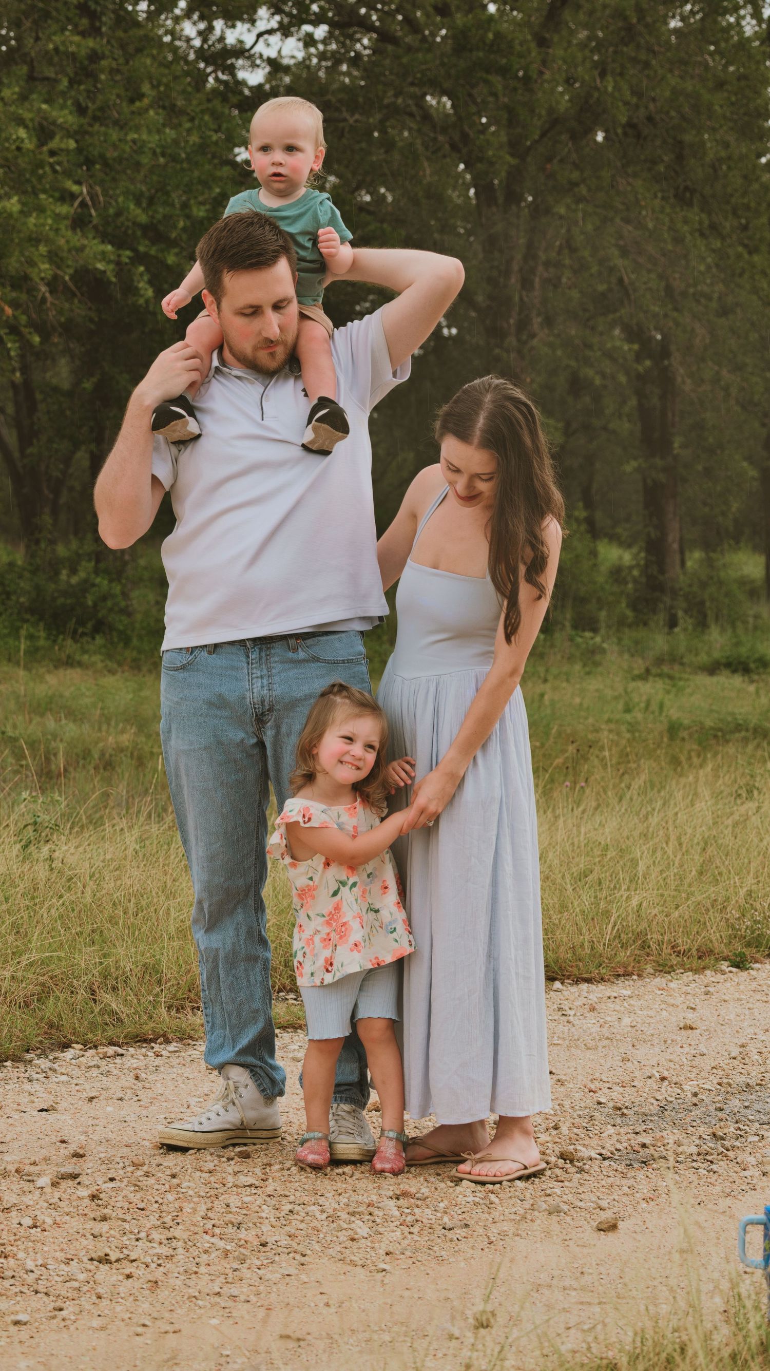 Active family of four walking on a dirt path through a green wooded area together.