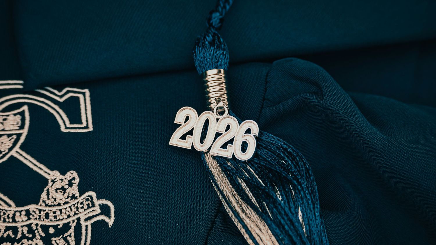 Close-up of a 2026 graduation tassel charm on a teal mortarboard cap for senior photos.