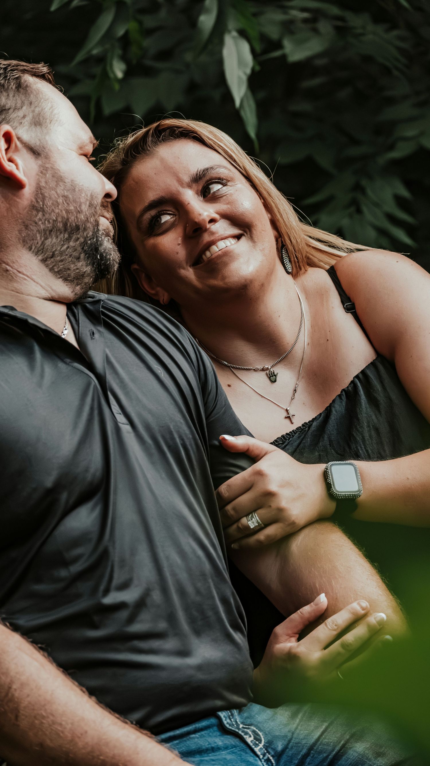 Couple sharing a romantic moment outdoors, smiling woman wearing an Apple Watch and engagement ring.