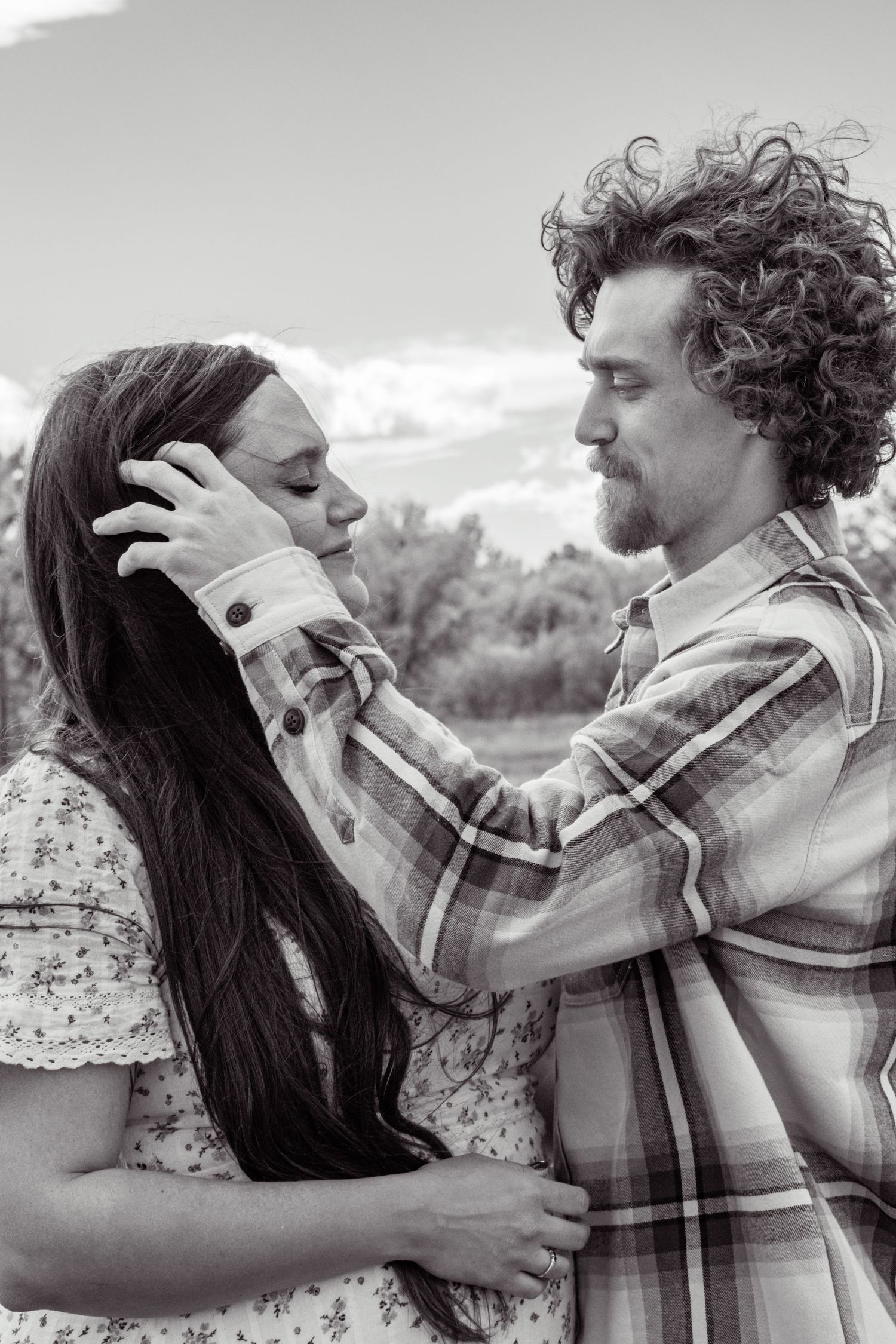 A black and white portrait of a couple facing each other, the man gently cradling the womans face.
