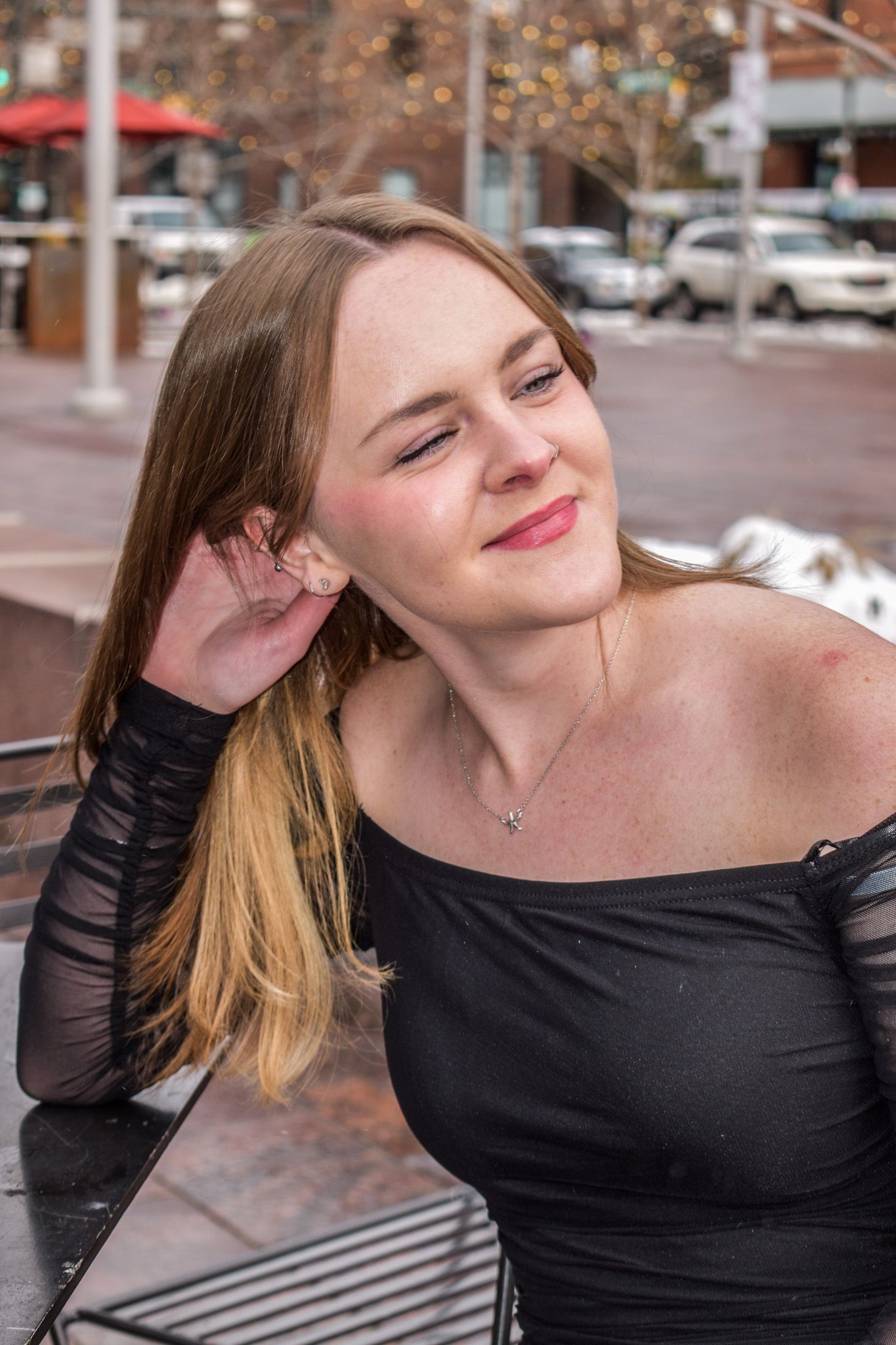 Smiling young woman with long blonde hair in black off-shoulder top posing outdoors in urban setting for senior photos.
