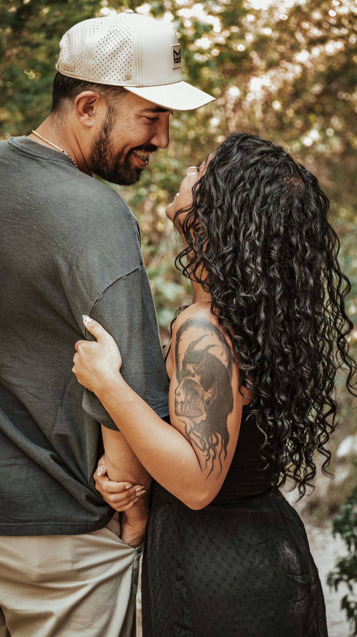 A smiling couple embraces outdoors, the woman looks up at her partner for a couples session.