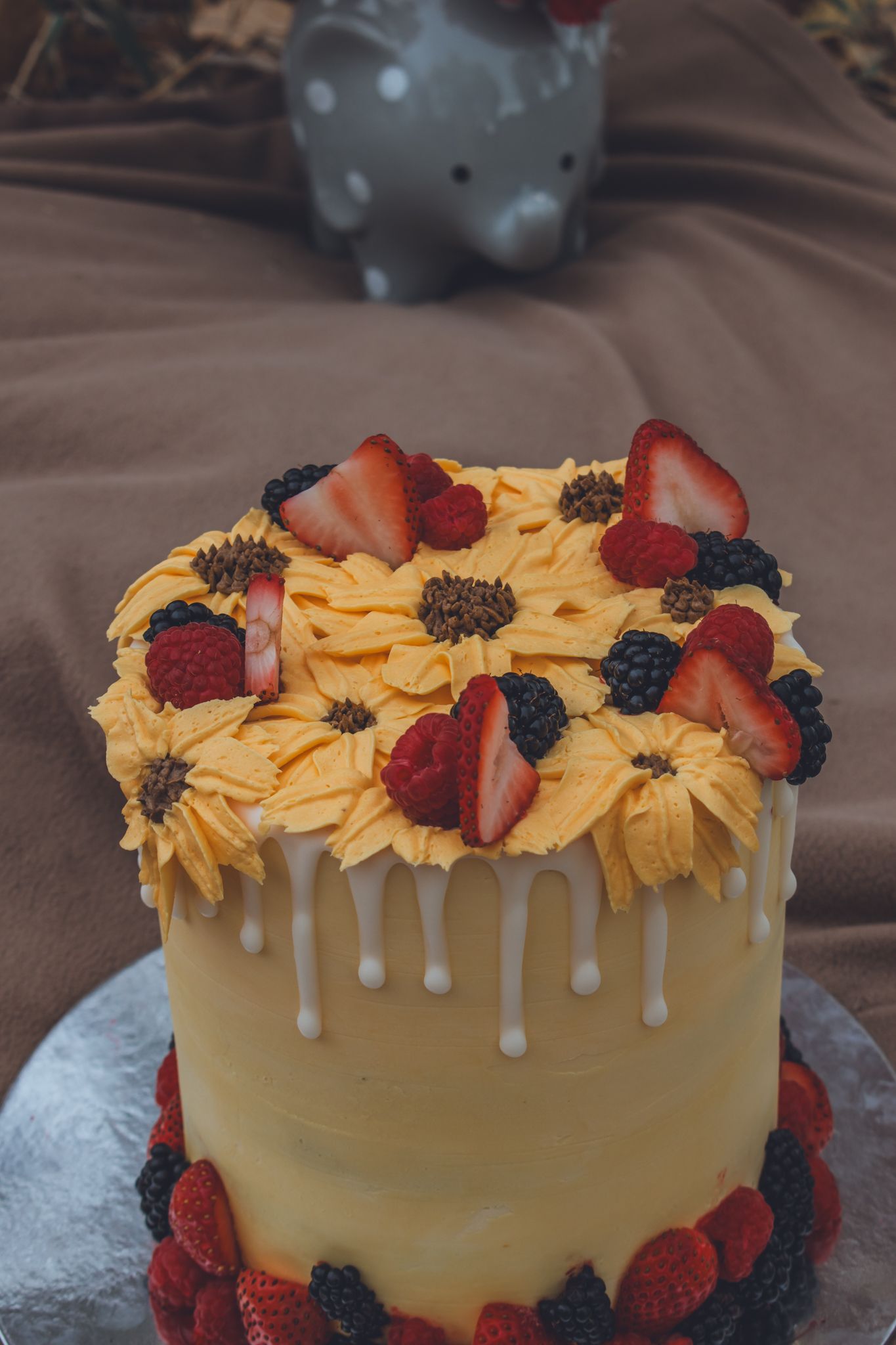 Elegant yellow birthday cake with sunflower frosting, fresh strawberries and blackberries on top. Family Photographer in Pflugerville, Tx